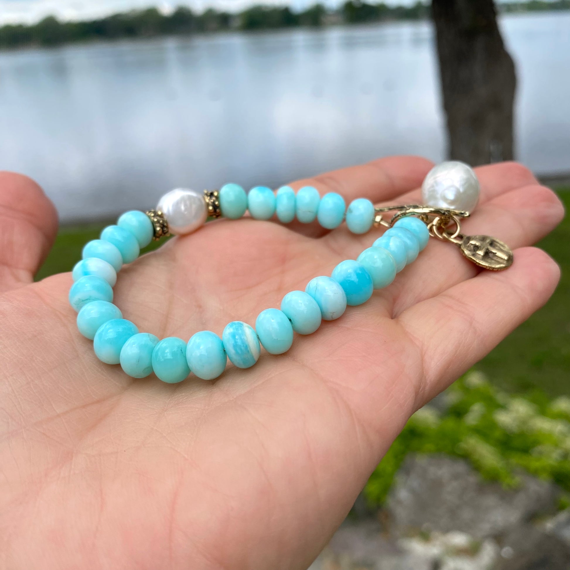 Sky blue opal bracelet with baroque pearls and cross charm, showcasing serene colors and artisan craftsmanship.