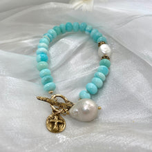 Load image into Gallery viewer, Sky blue opal bracelet with baroque pearls and cross charm on soft fabric background.
