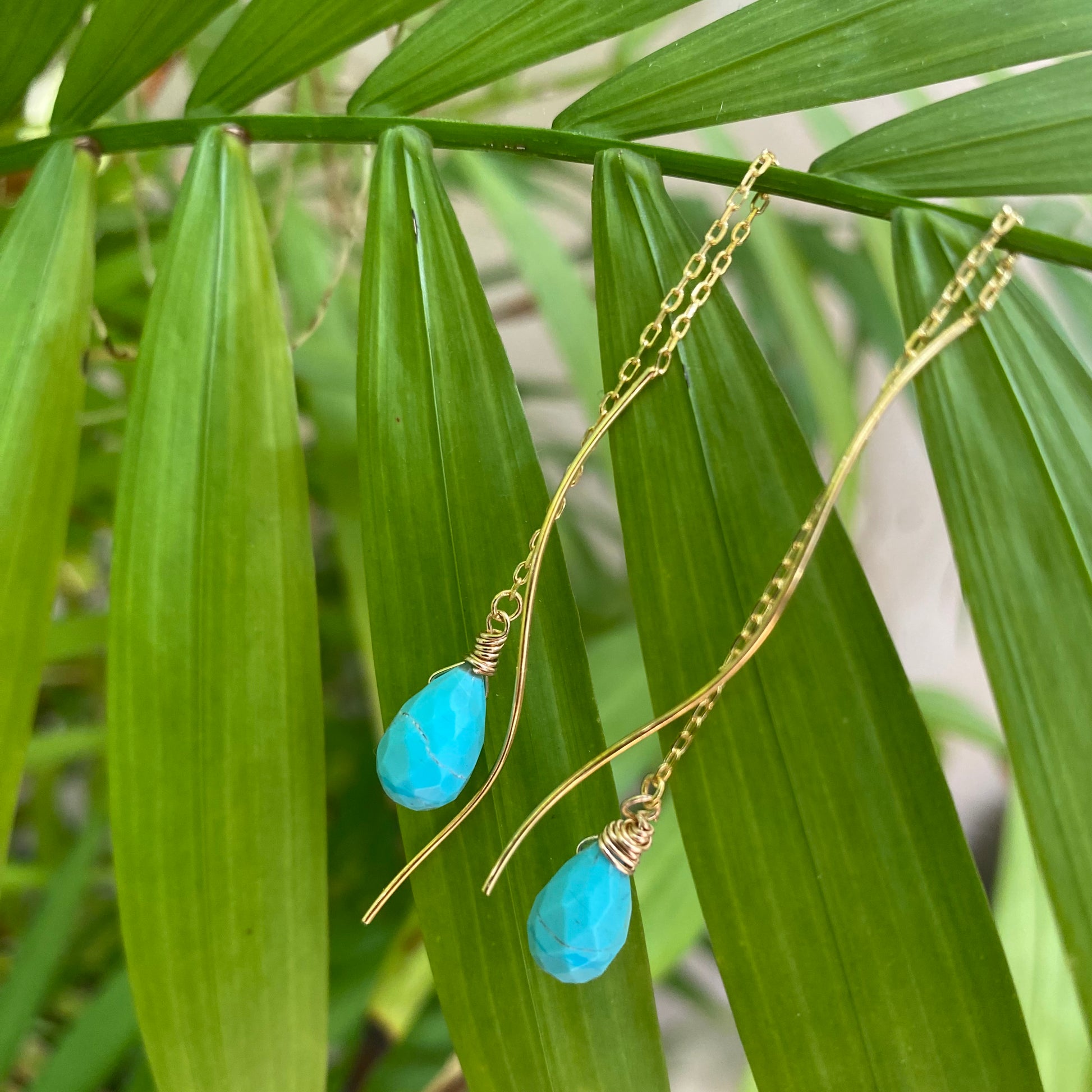 Turquoise threader earrings featuring Arizona briolettes on a backdrop of lush green leaves.