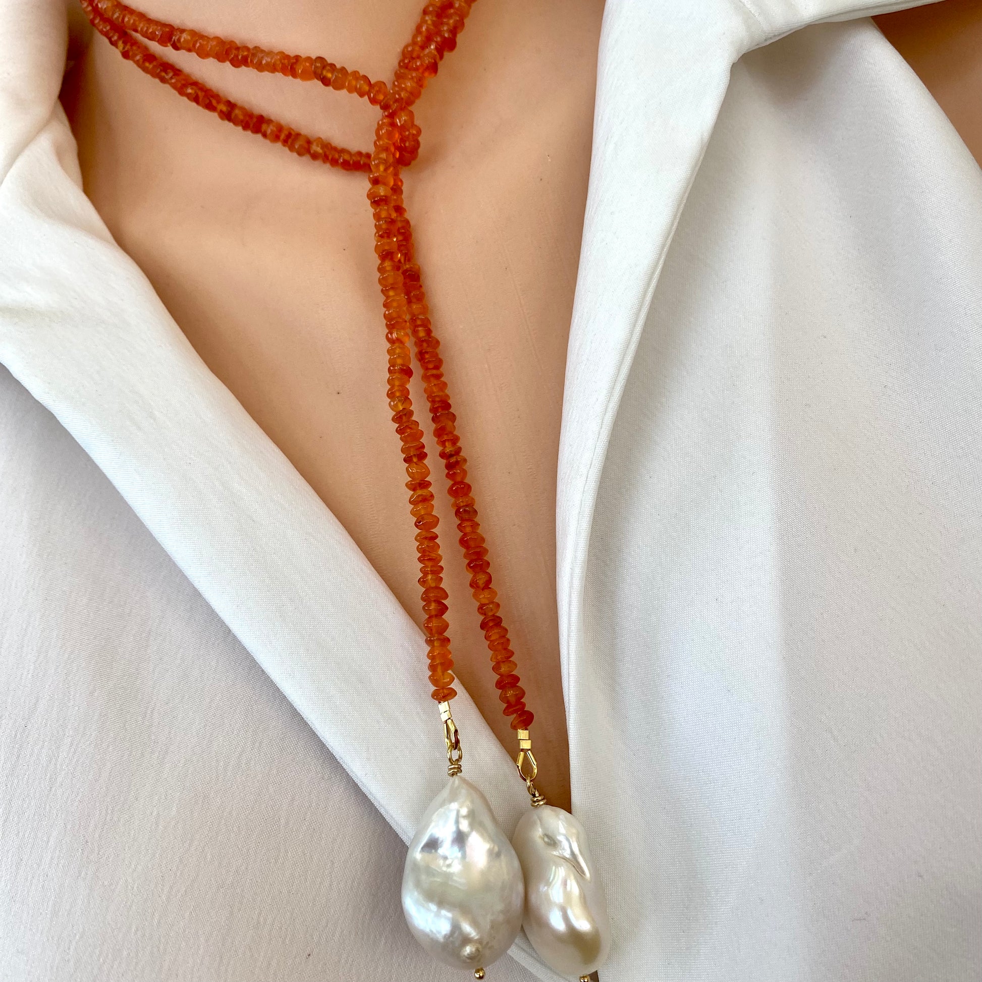 Close-up of a carnelian lariat necklace with two baroque pearls, elegantly worn over a white blouse.