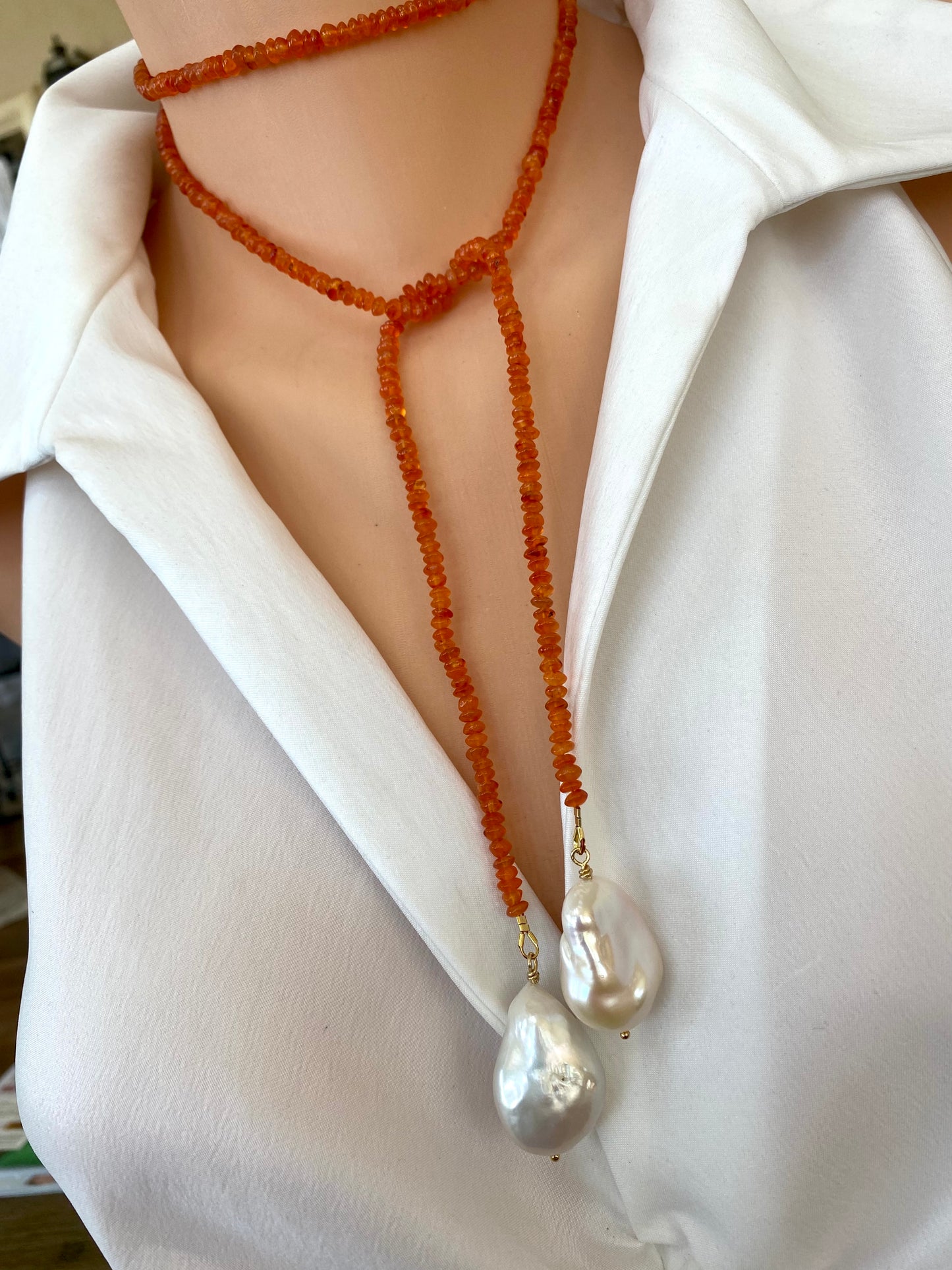 Carnelian lariat necklace featuring bright orange carnelian beads and two elegant baroque pearls, styled on a mannequin.