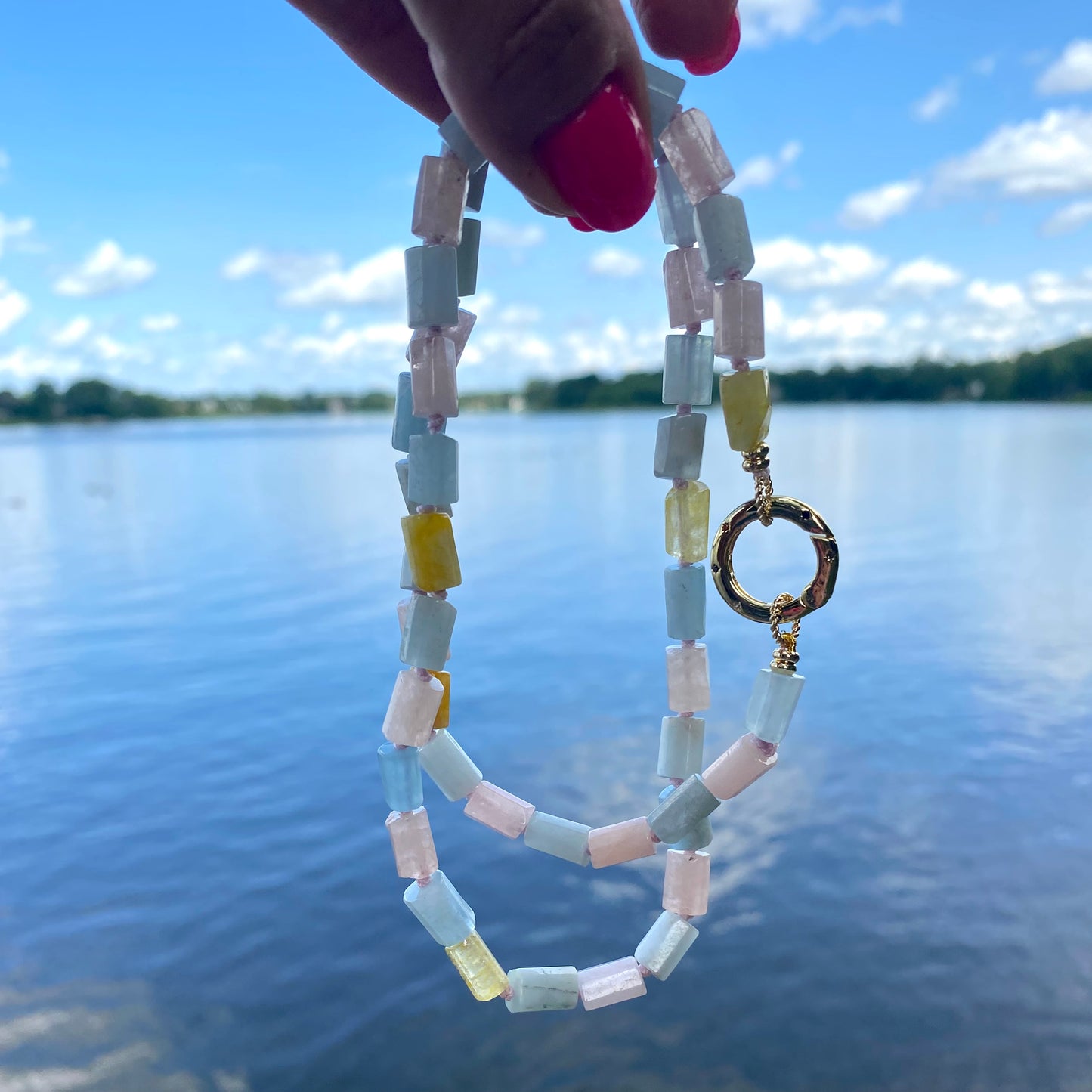 Beryl gemstone necklace featuring aquamarine, morganite, and heliodor against a scenic lake backdrop.