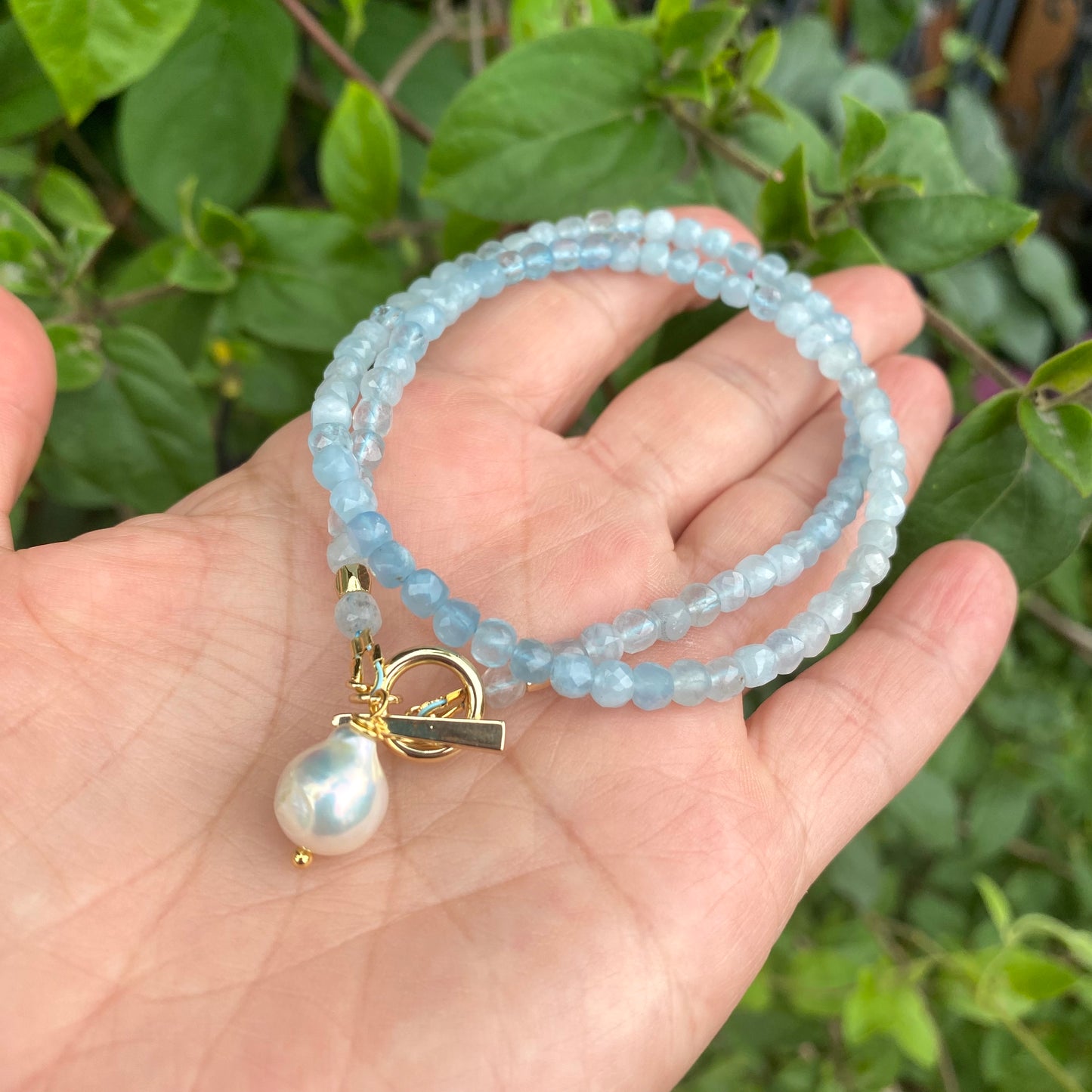 Aquamarine toggle necklace with baroque pearl pendant held in hand, showcasing delicate craftsmanship and soothing blue tones.