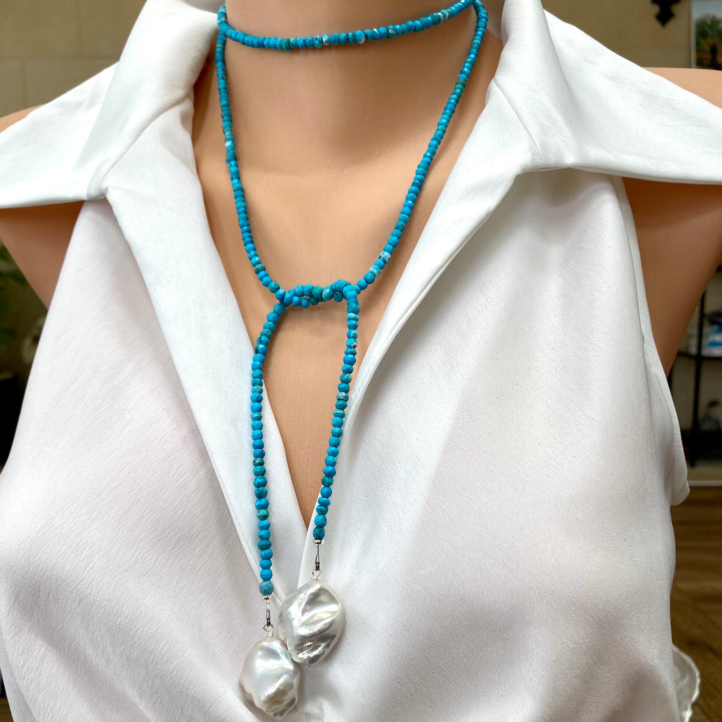 Turquoise lariat necklace with two baroque pearls elegantly displayed on a mannequin wearing a white shirt.