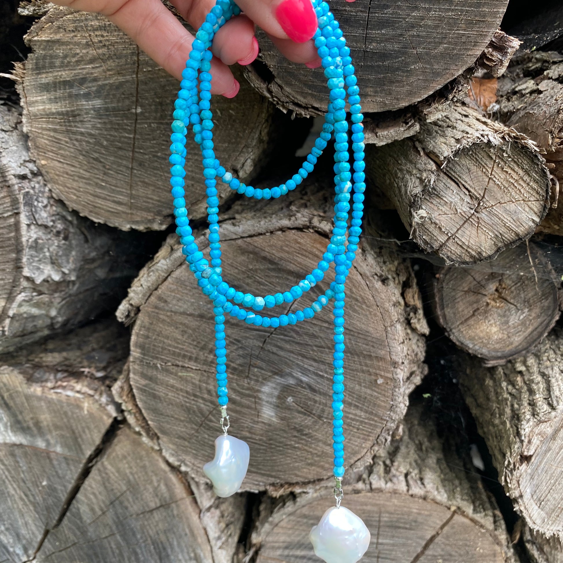 Turquoise lariat necklace with two baroque pearls showcased against wooden logs