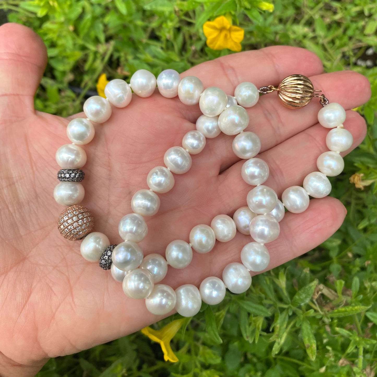 Close-up of rose gold pearl necklace showing pearls and black rhodium silver details on leaf background.