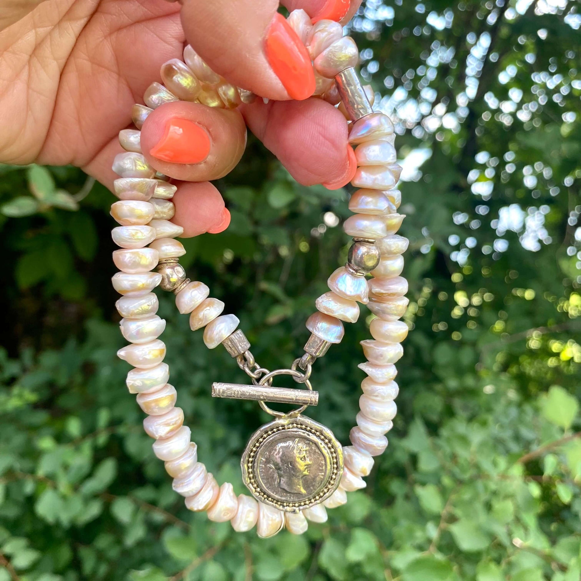 Lavender baroque pearl necklace featuring silver Roman coin toggle clasp in a natural setting.