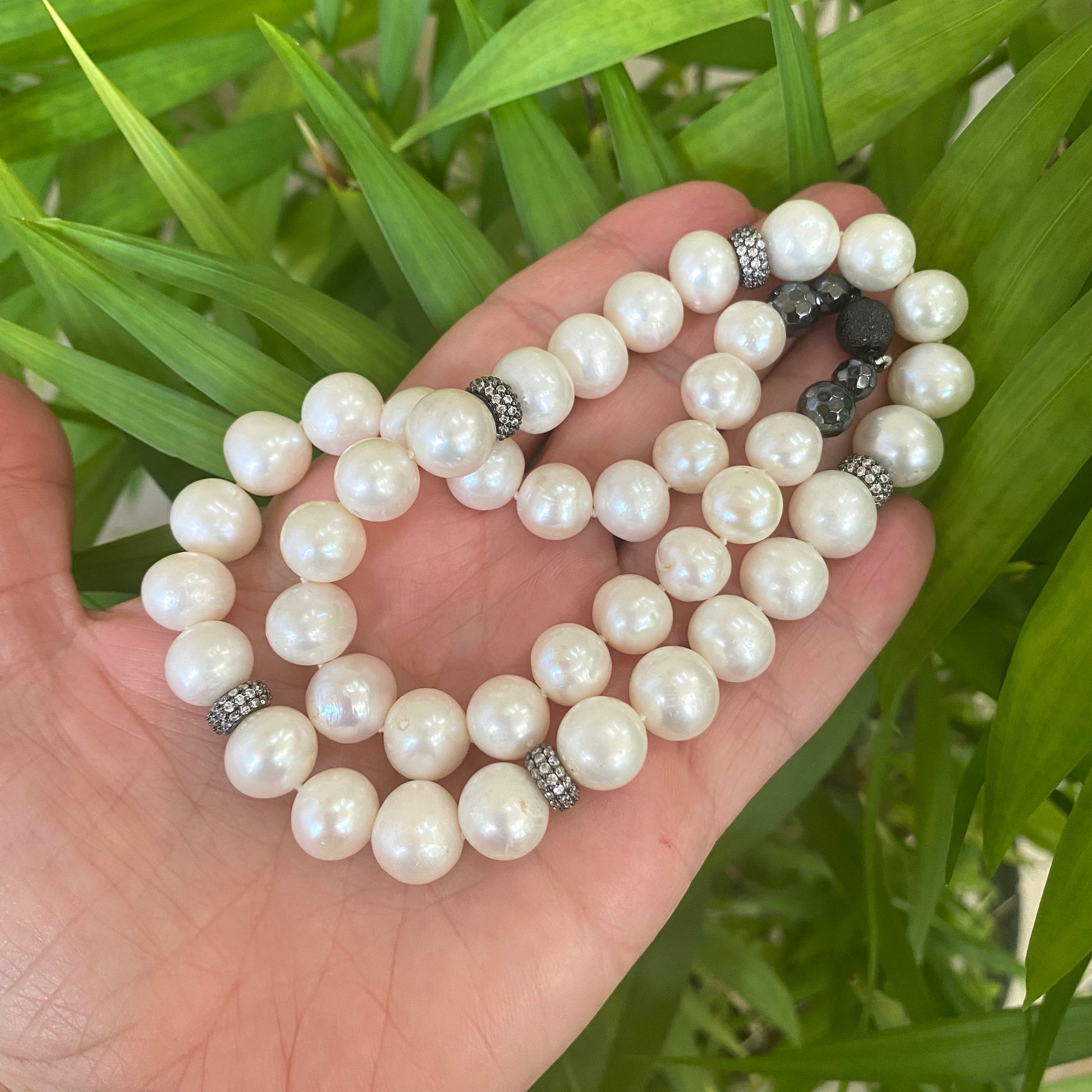 Handmade pearl necklace with zircon pave beads displayed on a hand, showcasing lustrous white freshwater pearls.