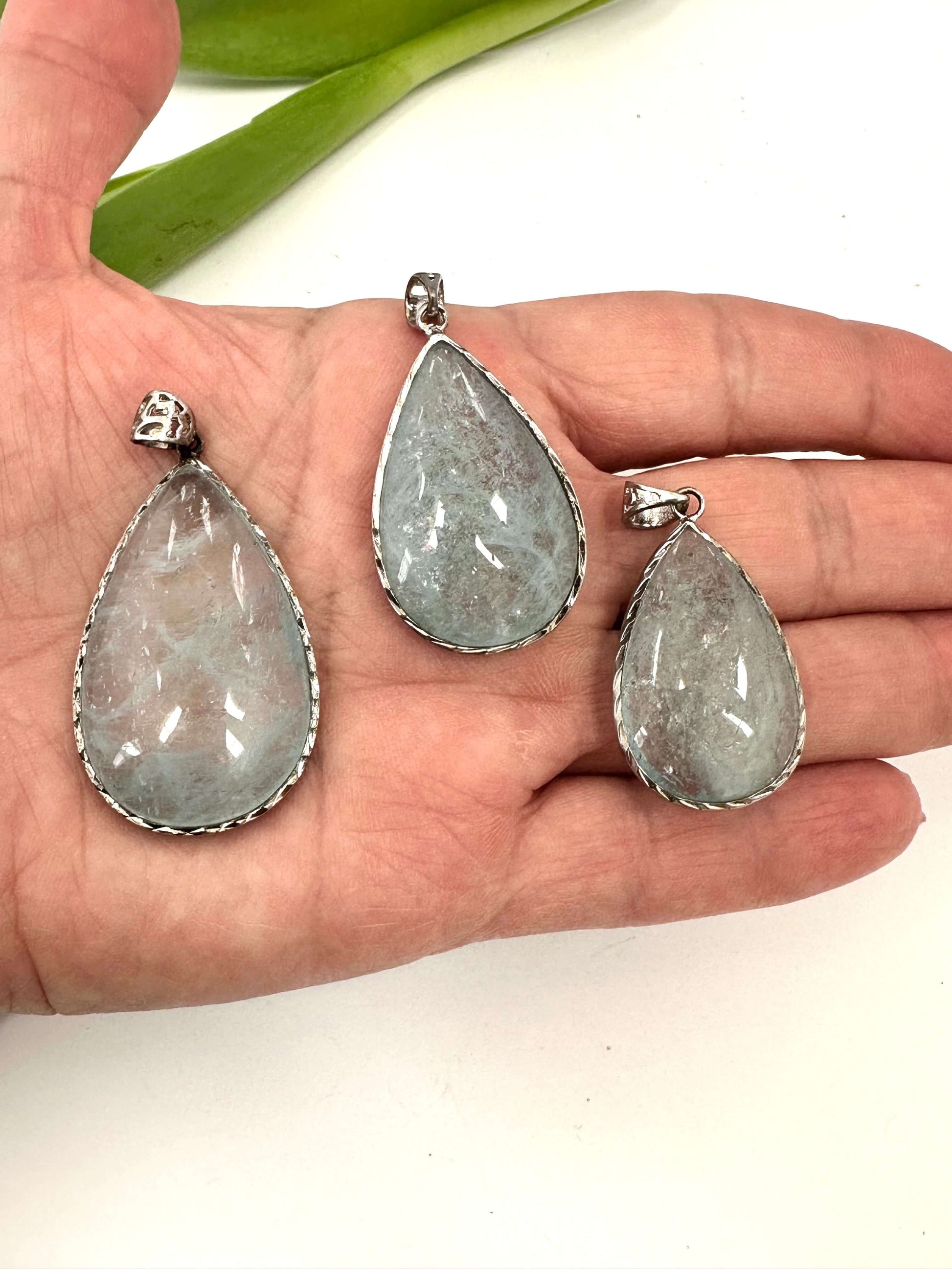 Aquamarine teardrop pendant in oxidized sterling silver displayed in hand, featuring three pear-shaped aquamarine stones.
