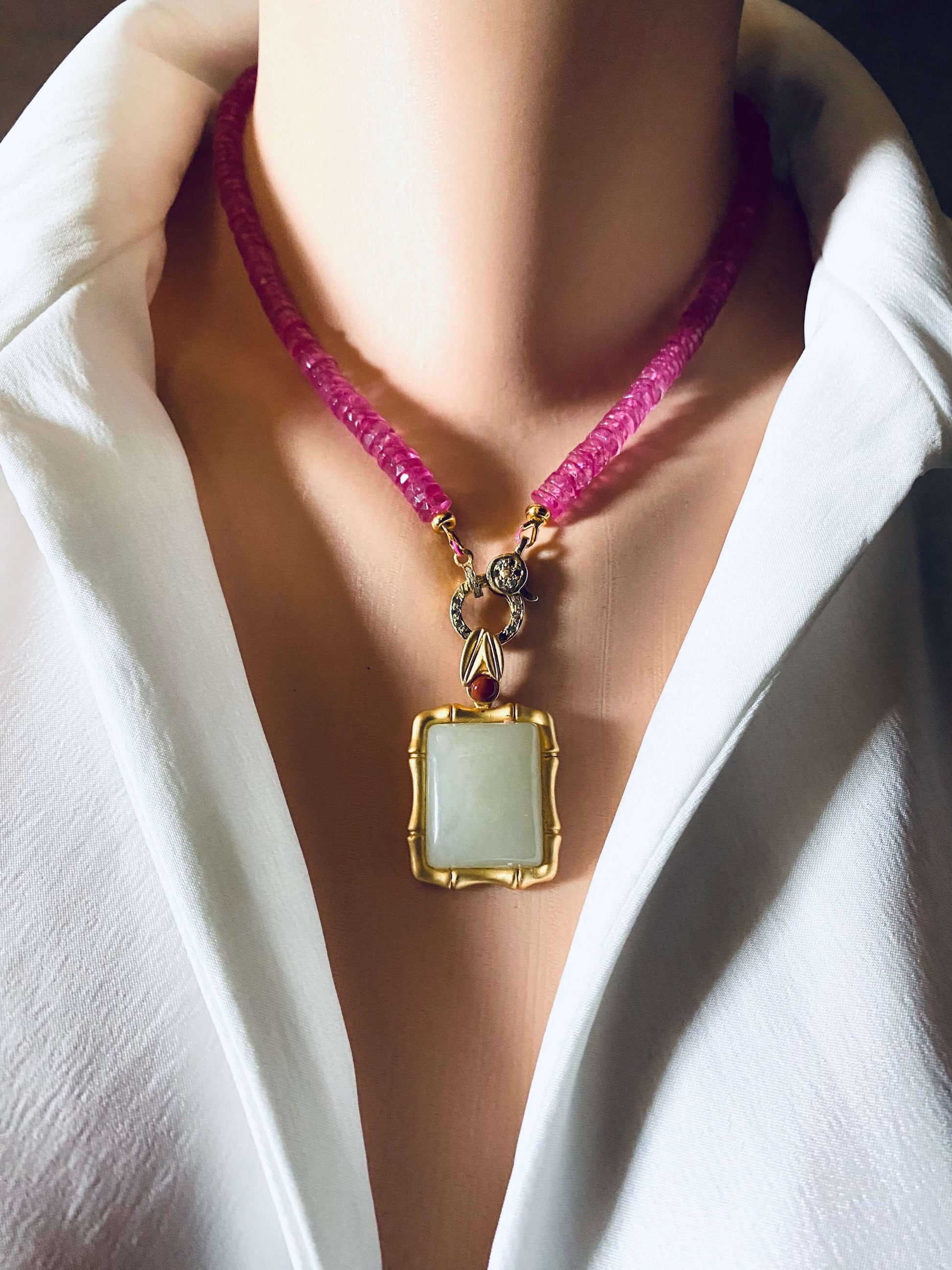 Bamboo style jade pendant with red agate in gold vermeil showcased on a model's neck with a pink necklace.