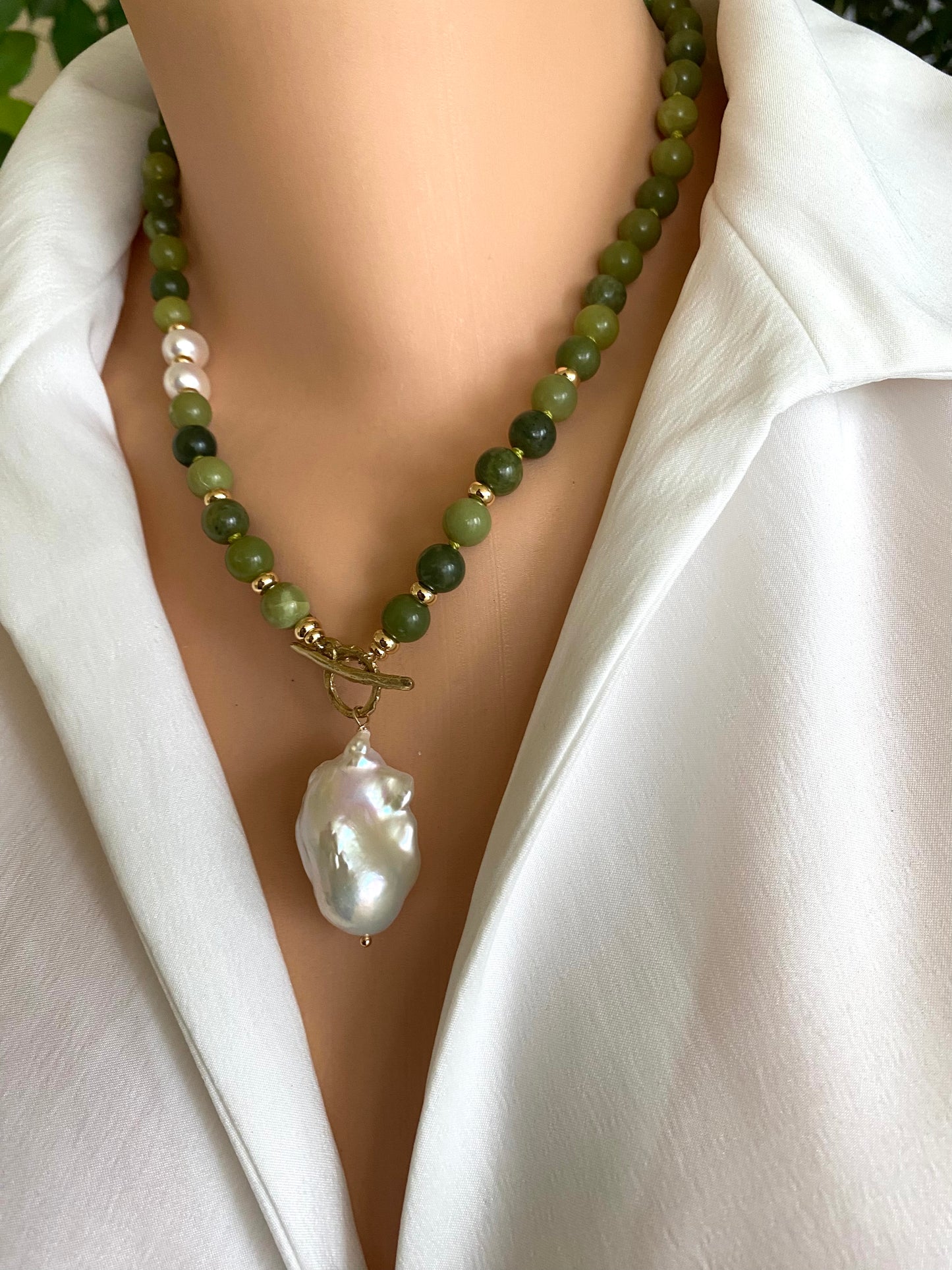 Necklace with green beads and a large white pearl pendant on a mannequin wearing a white shirt.