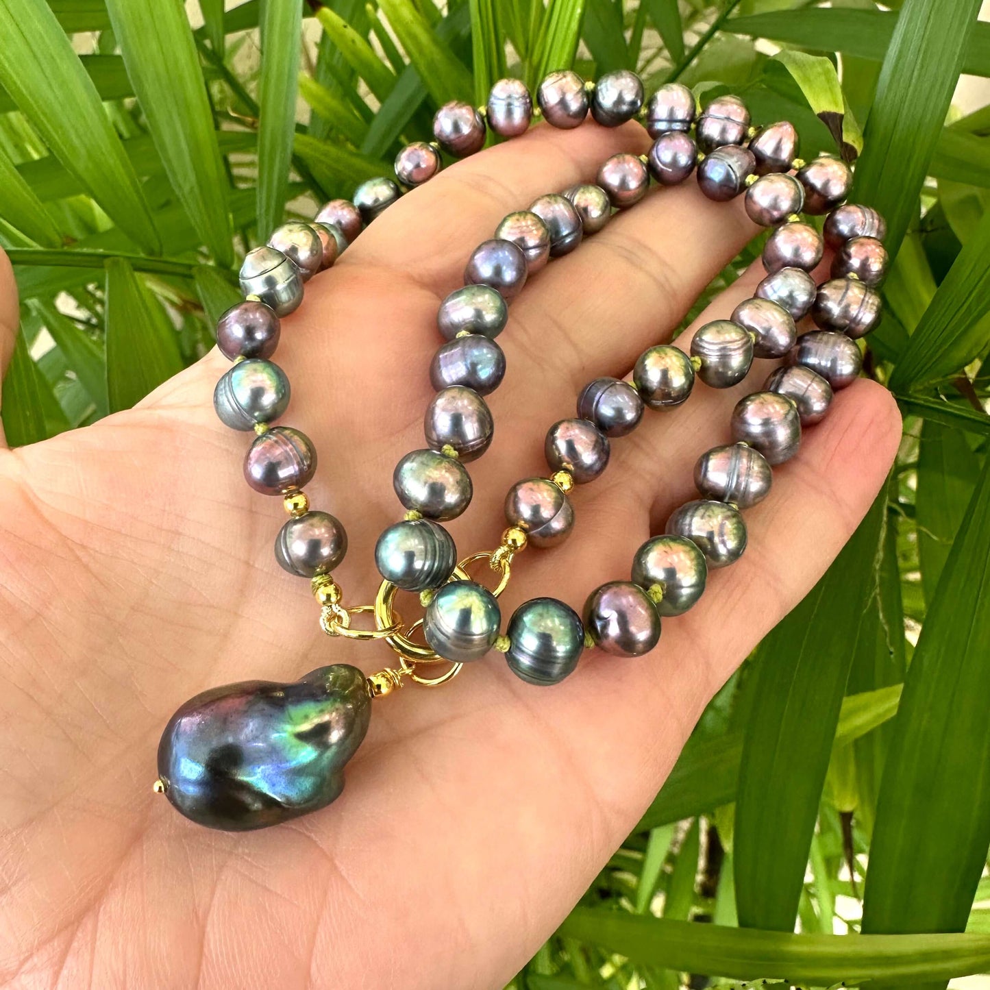 Black pearl pendant necklace held in hand for scale against green leaf background