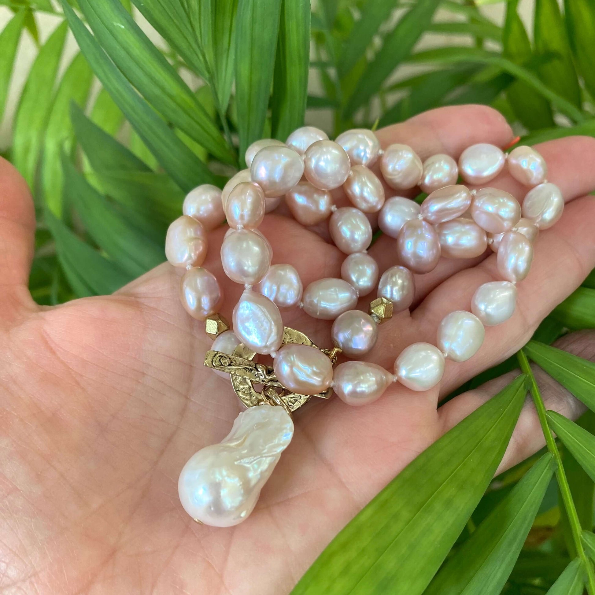 Close-up of pink pearl necklace held in hand near green foliage