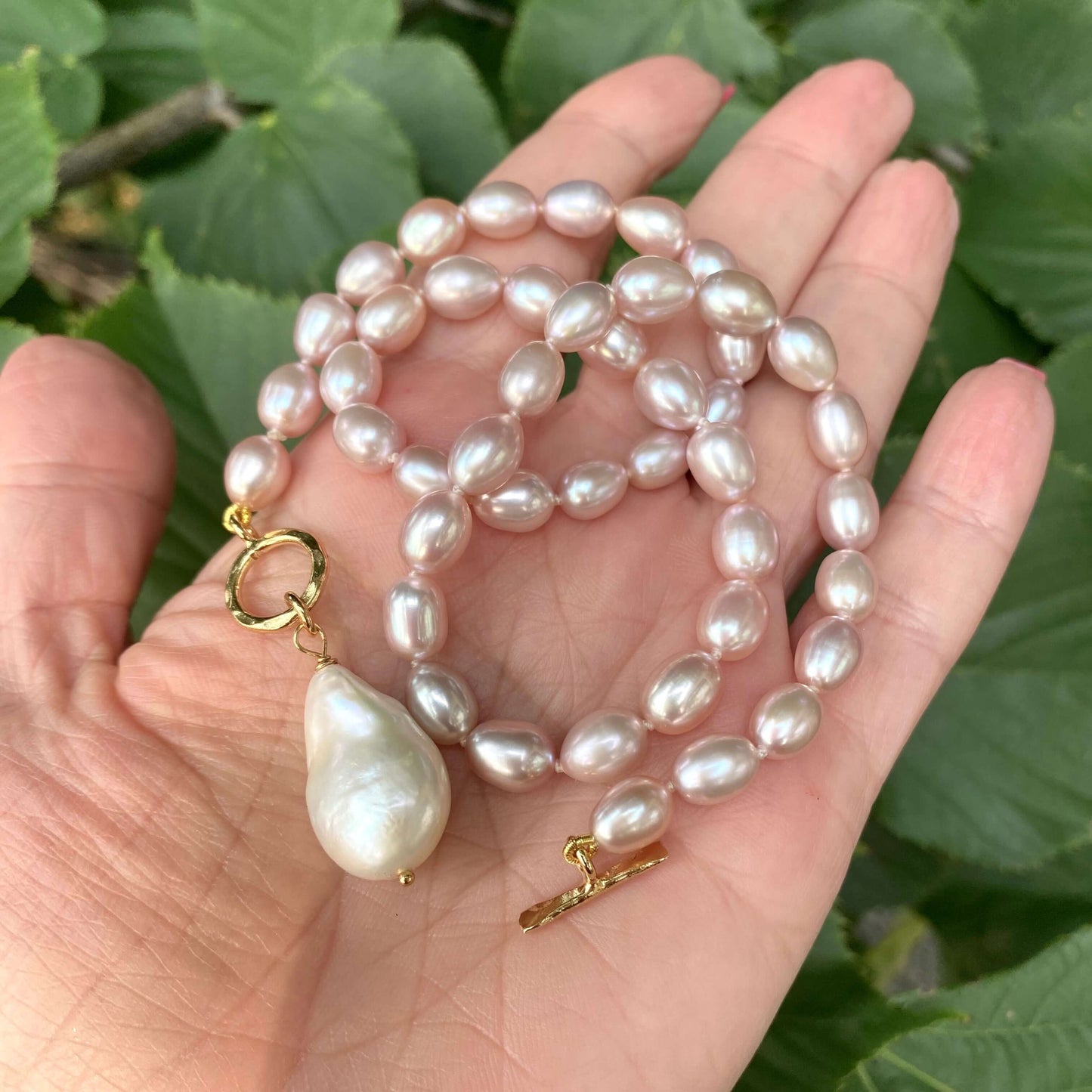 Pink pearl toggle necklace with baroque pearl held in hand showing soft pink pearls and white pendant
