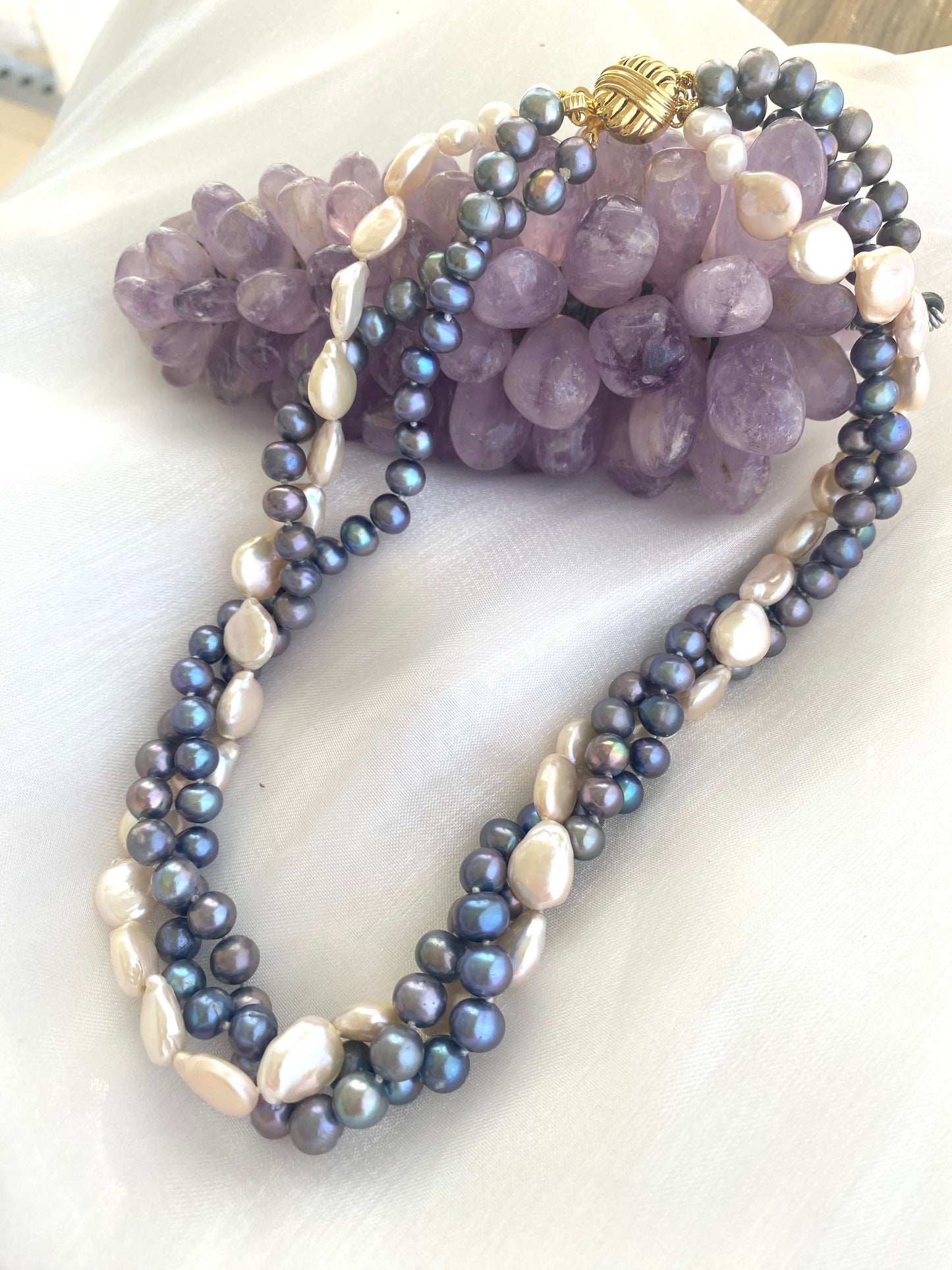 Black and White Pearl Necklace laid beside amethyst ornament on white background showcasing contrast of pearls.