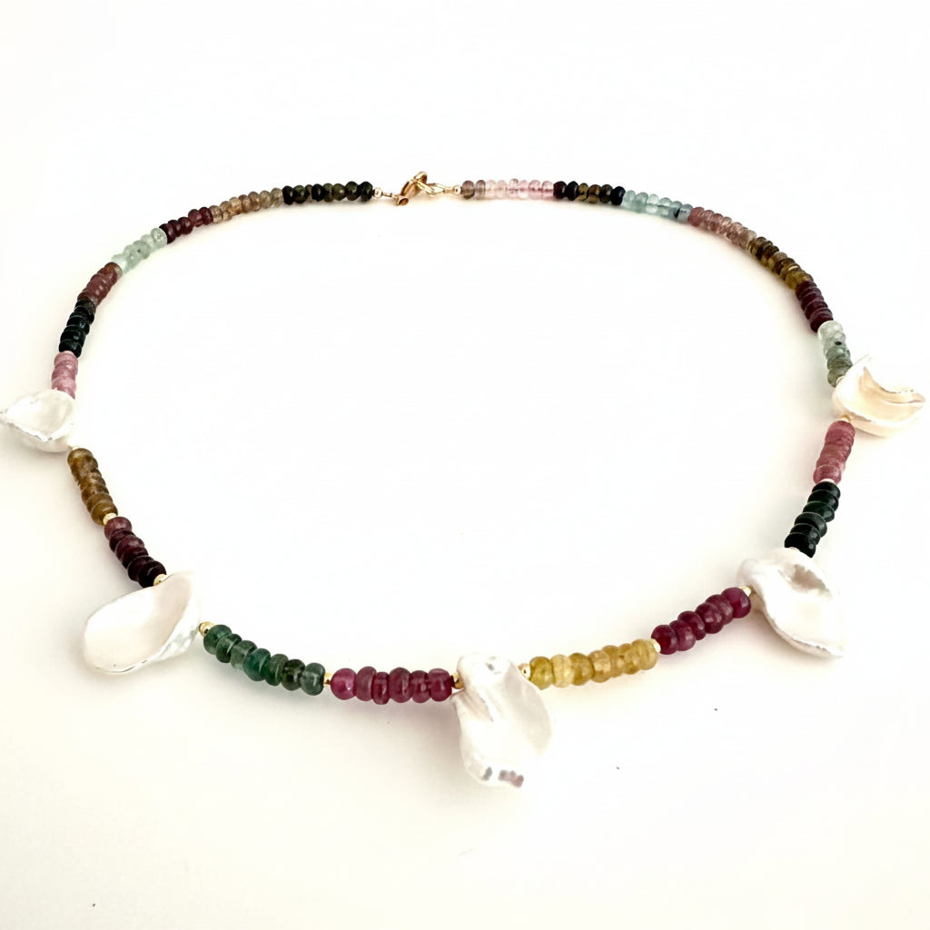 A beaded necklace featuring small multicolored gemstone beads and several white shell charms, displayed on a plain white background.