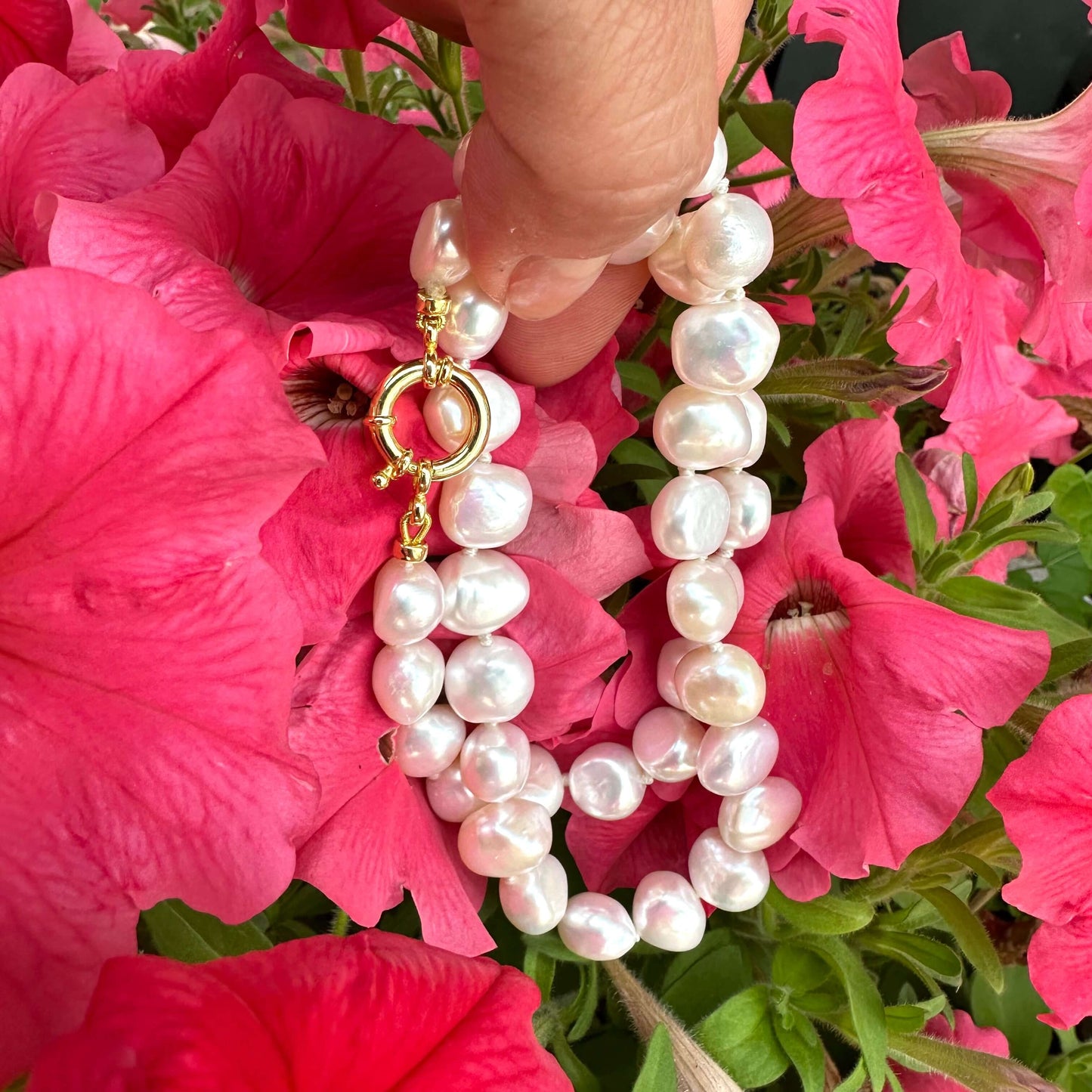 Hand holding a small baroque pearl classic necklace against vibrant pink flowers.