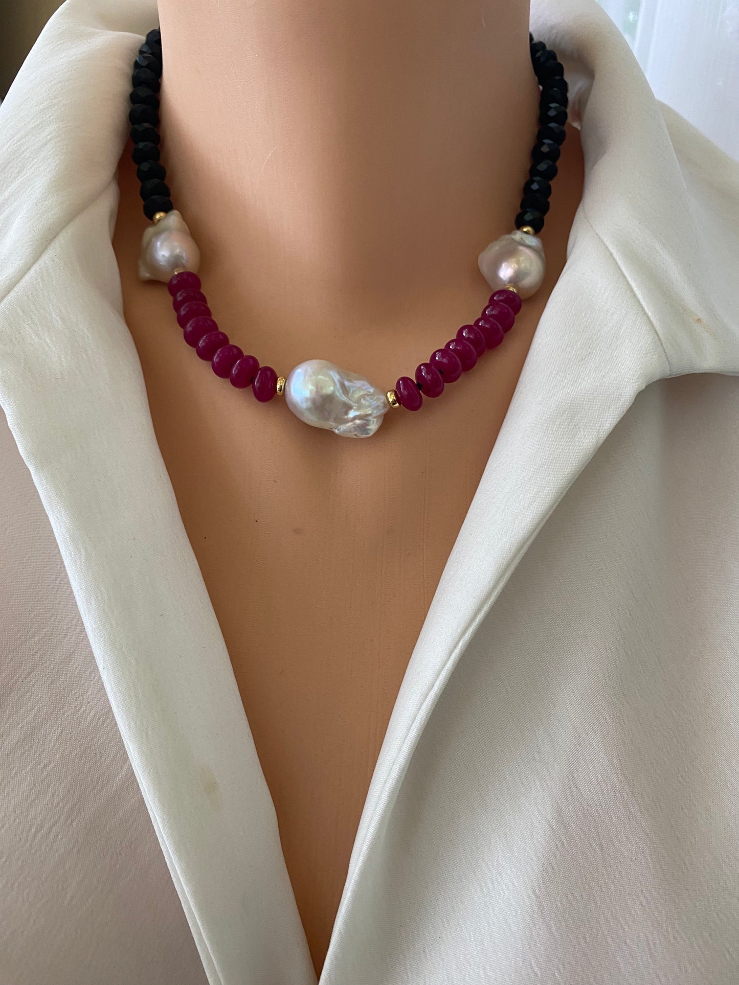 Necklace with black, red, and pearl beads on a mannequin wearing a white jacket.
