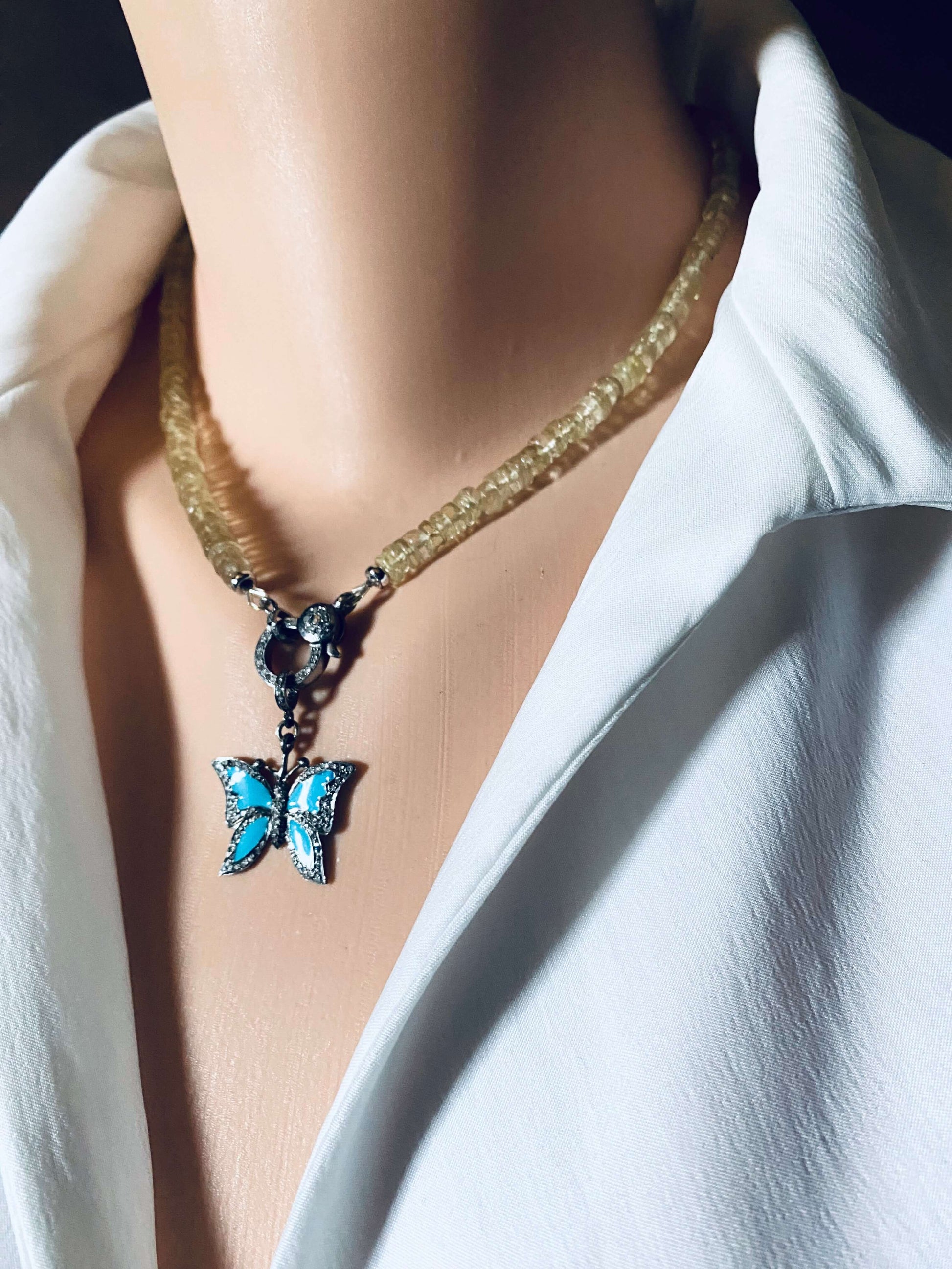 Blue enamel butterfly pendant with diamond pavé hanging from a necklace on a mannequin's neck.