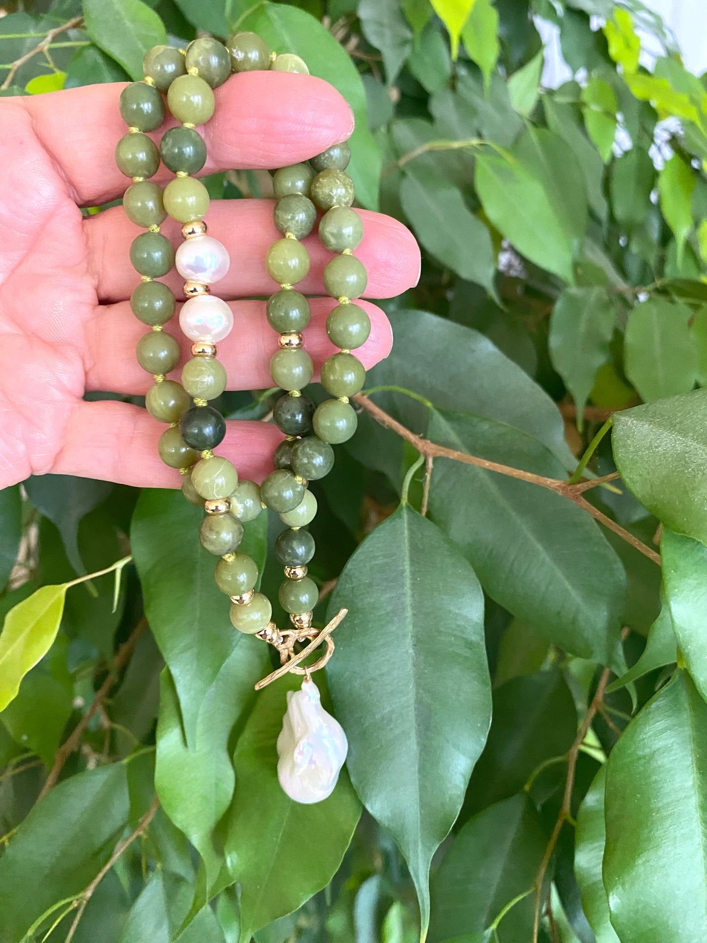 Hand holding a green beaded necklace with leaves in the background