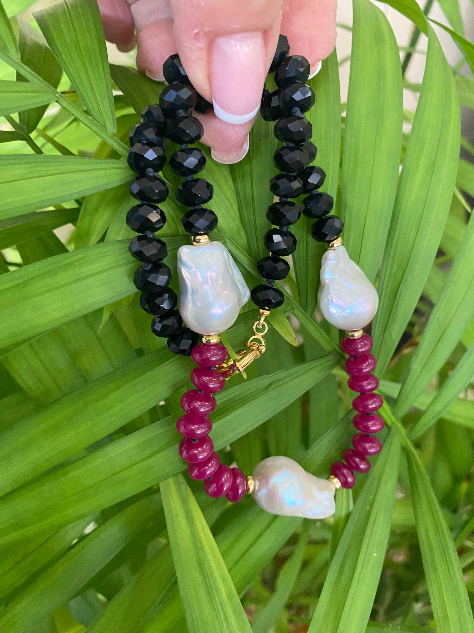 Black, red, and white beaded bracelet held over green leaves