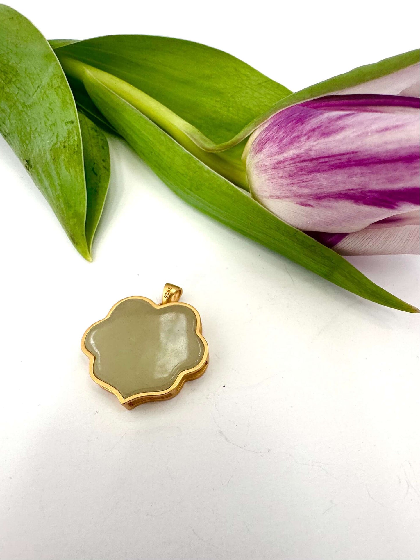 Hotan jade pendant in gold vermeil on a white surface with tulip and leaf, showcasing natural nephrite charm.