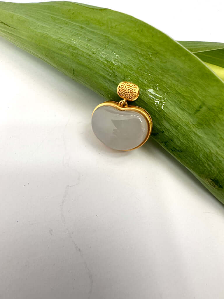 Hotan jade charm pendant in gold bezel showcasing natural nephrite jade on a green leaf background.