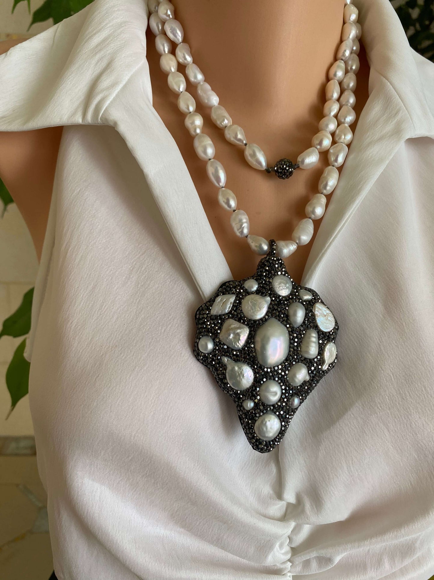 Long white pearl nugget necklace with pavé pendant displayed on a model wearing a white blouse.