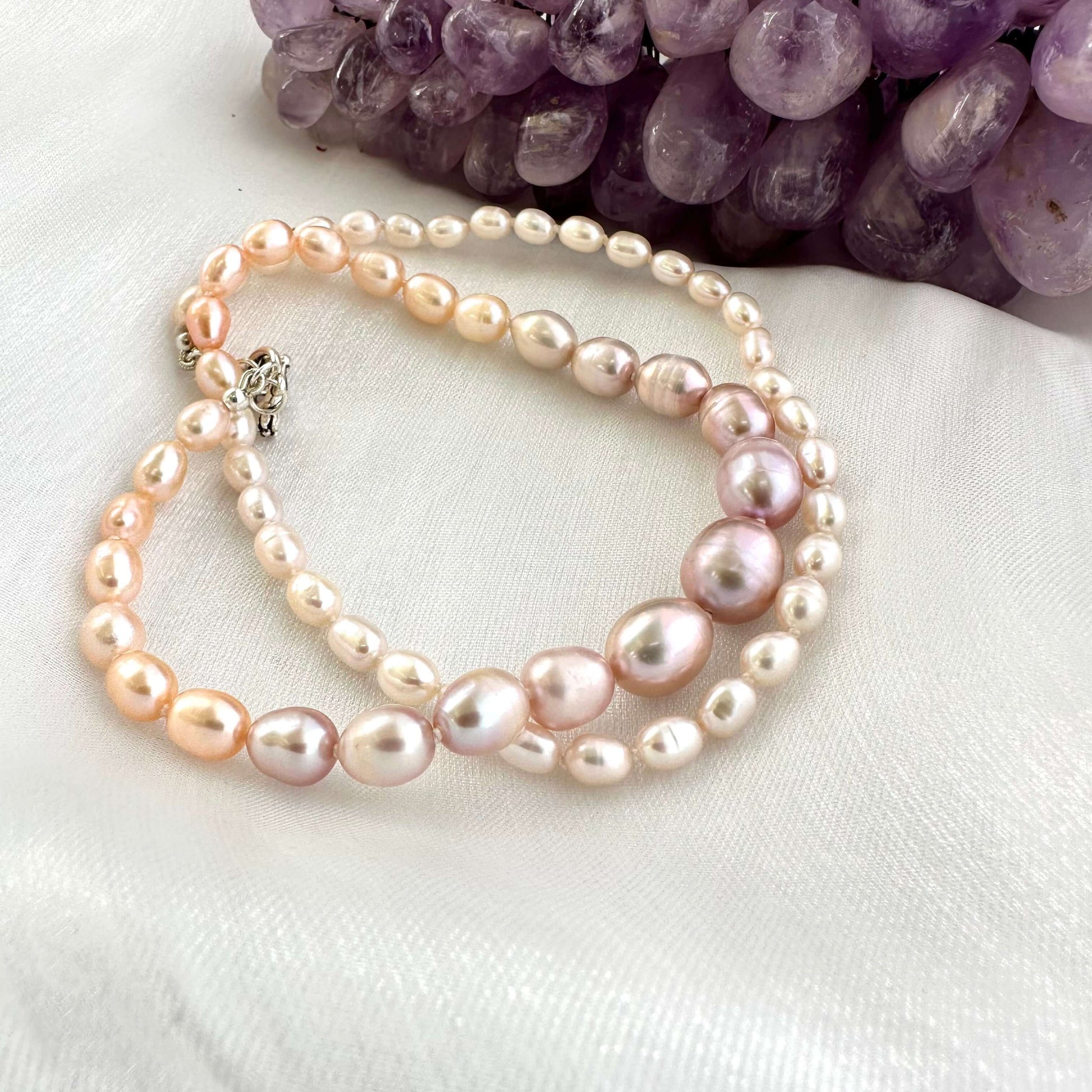 Close-up of Rice Pearl Necklace showing pastel freshwater pearls beside amethyst stone on white cloth.