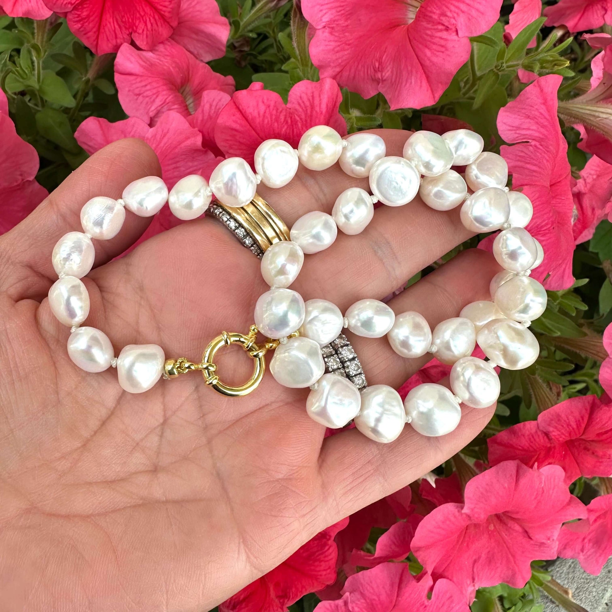 Small baroque pearl classic necklace displayed on a hand, surrounded by colorful pink flowers.
