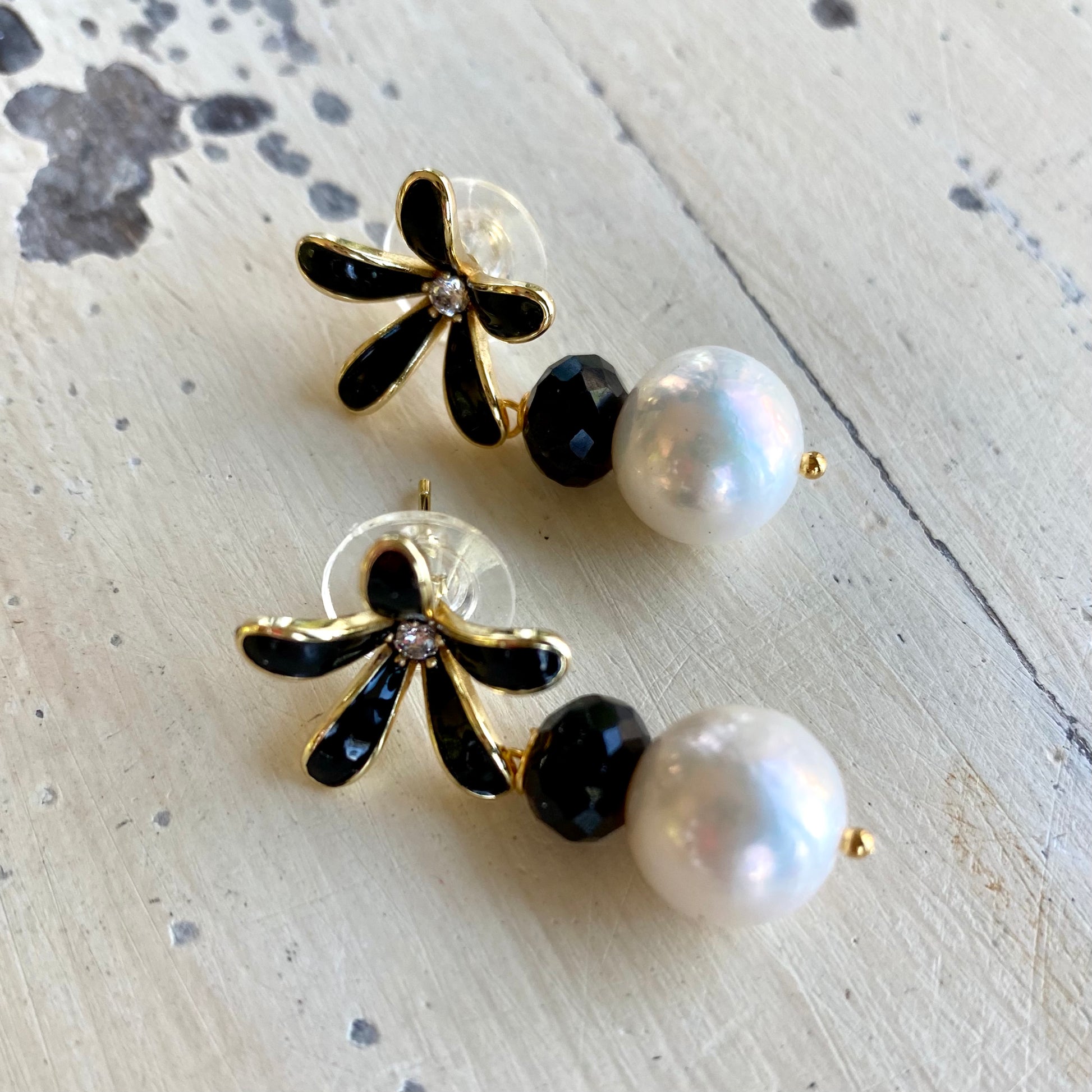 Edison pearl black spinel earrings on tabletop, pair of pearl drops with black enamel flower studs