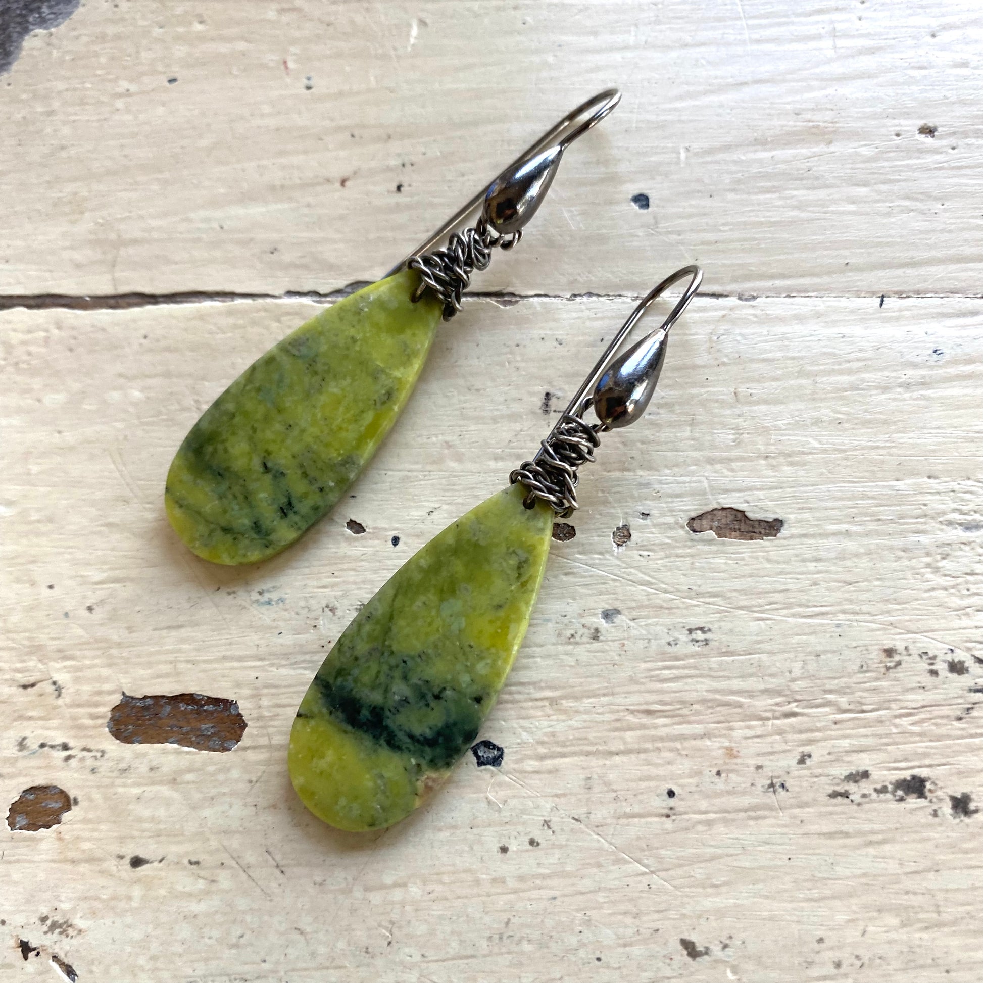 Green serpentine teardrop earrings with black rhodium silver wire on light wood background