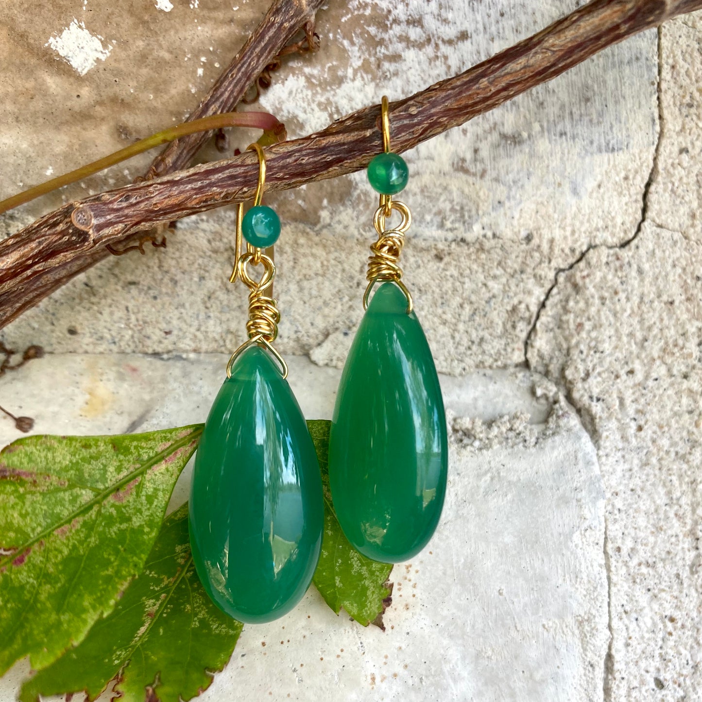 Emerald green onyx teardrop earrings displayed on stone showing polished green gemstones