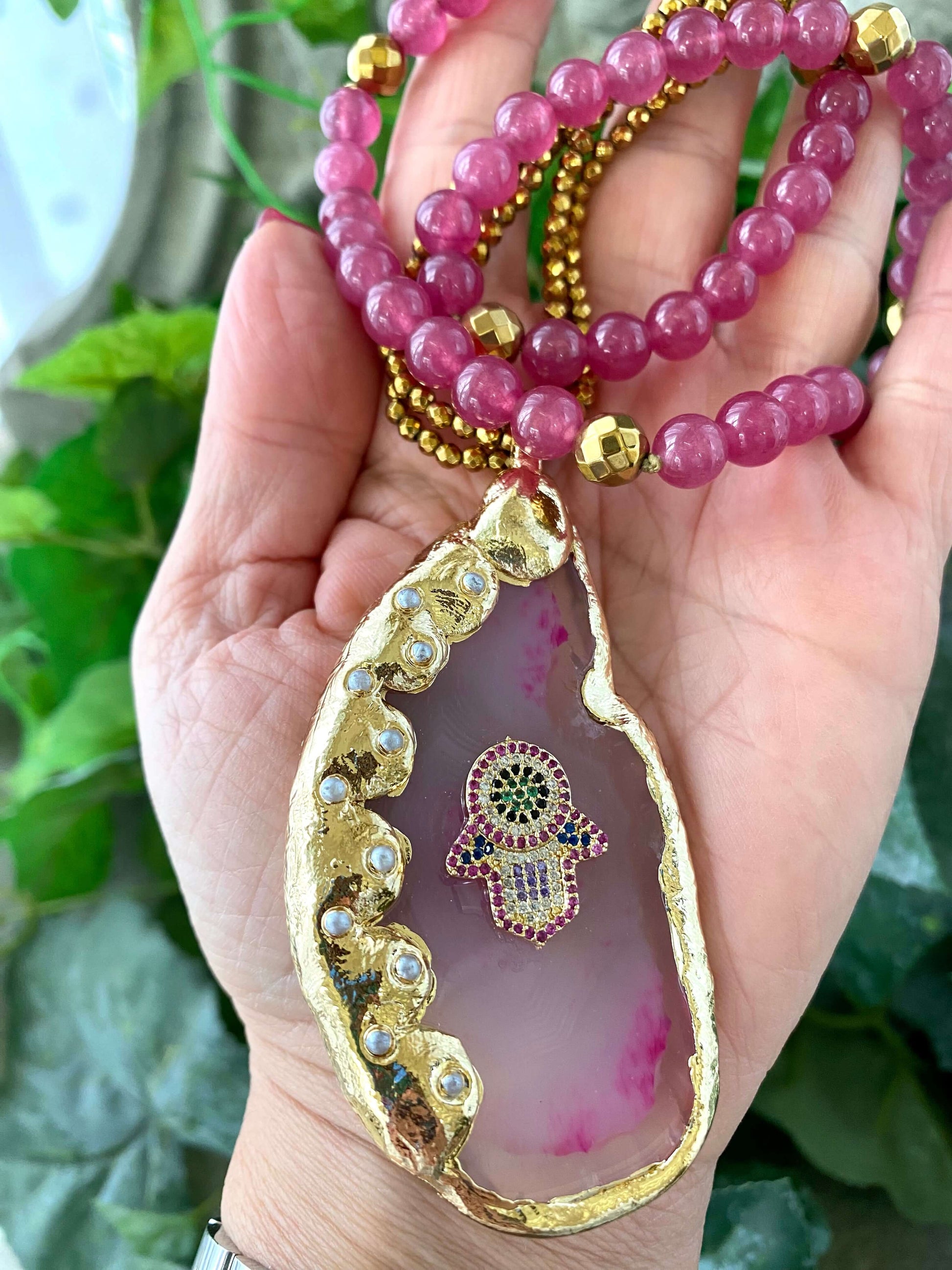 Hot pink agate pendant necklace featuring a gold-electroplated Hamsa symbol with colorful beads.