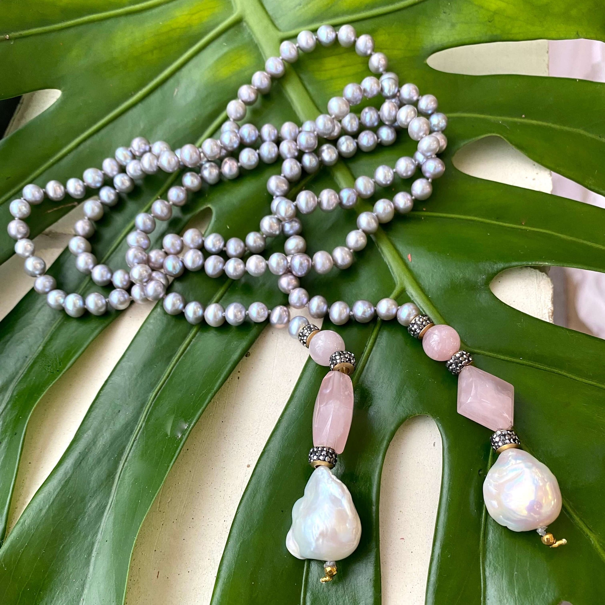 Pastel pearl lariat necklace featuring blue-gray freshwater pearls and pink rose quartz on a green leaf background.