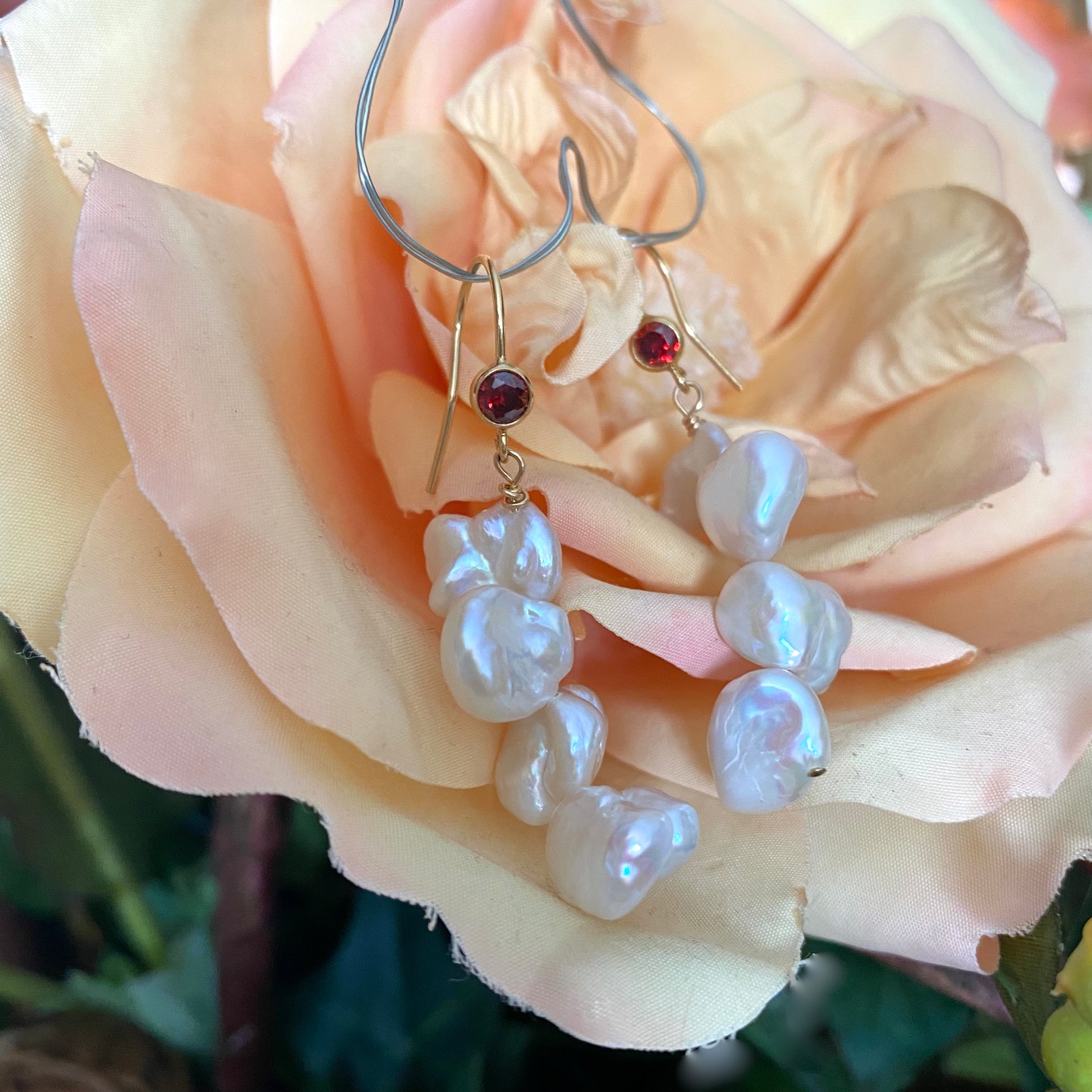 Pearl drop earrings with keshi pearls and red CZ, showcasing unique elegance against a soft rose background.
