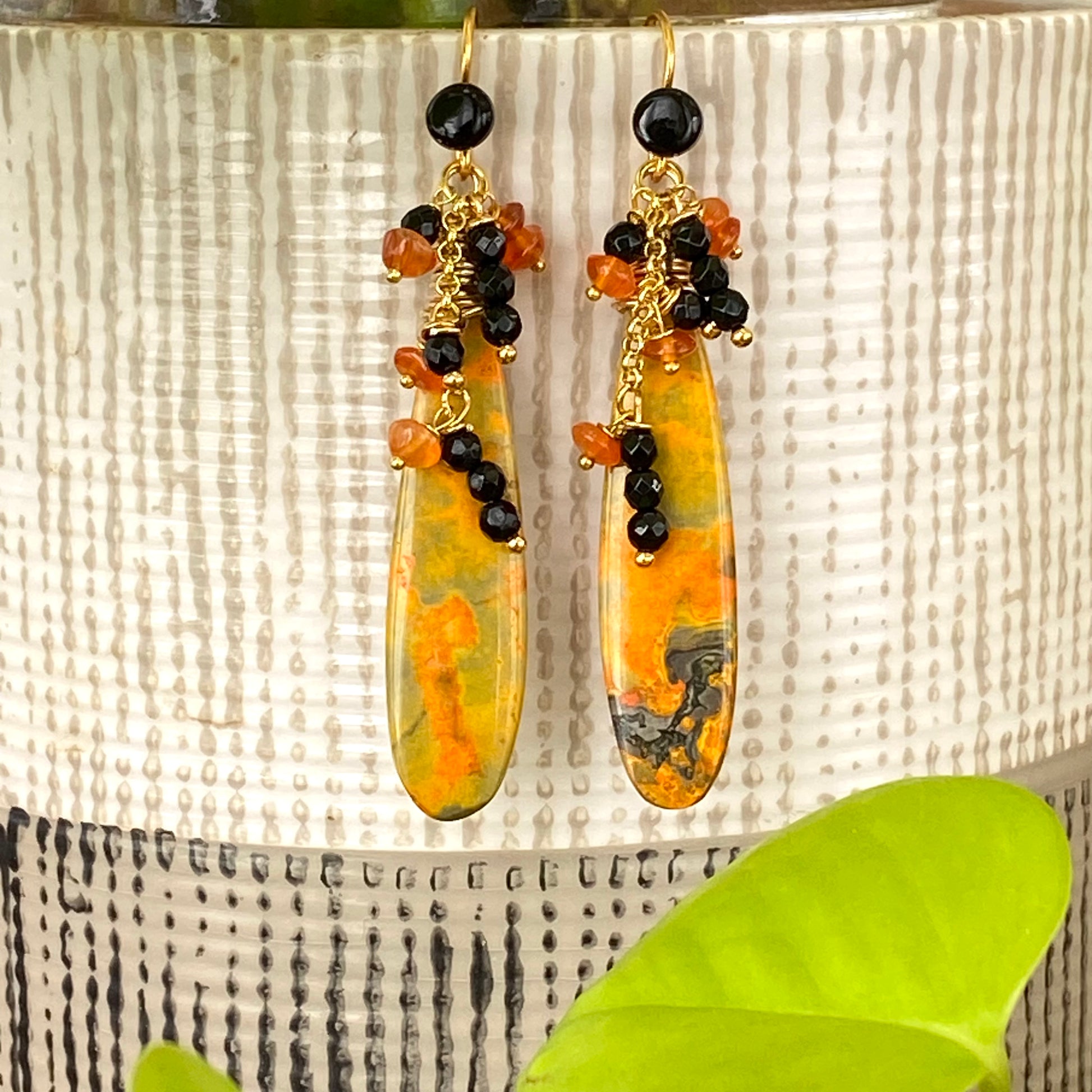 Bumble Bee Jasper earrings with carnelian and onyx clusters hanging against a decorative background.