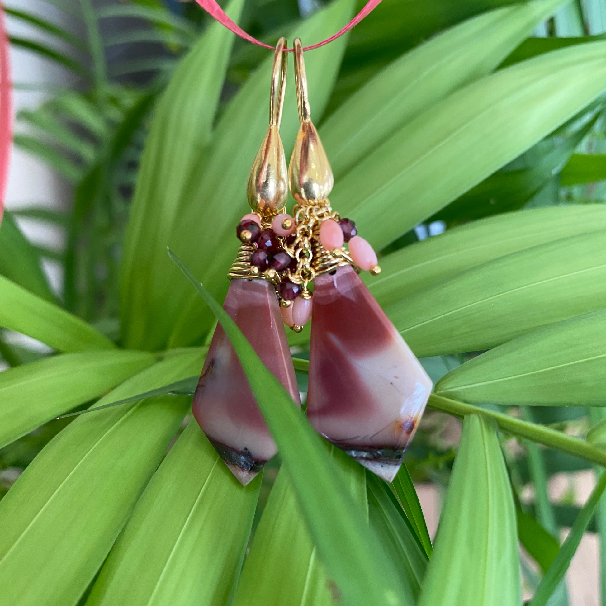 Jasper cluster earrings with Mookaite, Garnet and Pink Coral hanging elegantly against green foliage.
