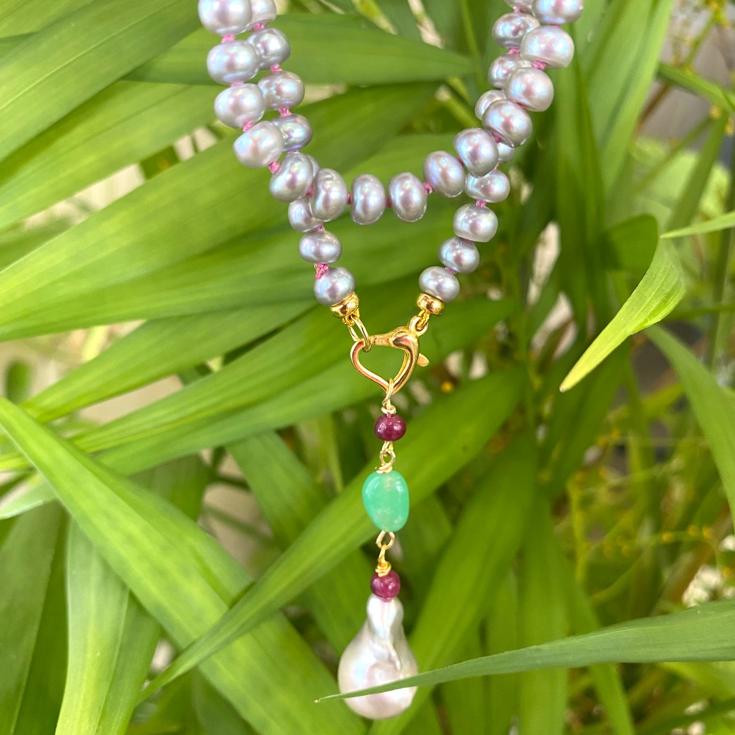 Grey pearl necklace with ruby and chrysoprase pendant on a green background, showcasing elegant craftsmanship.