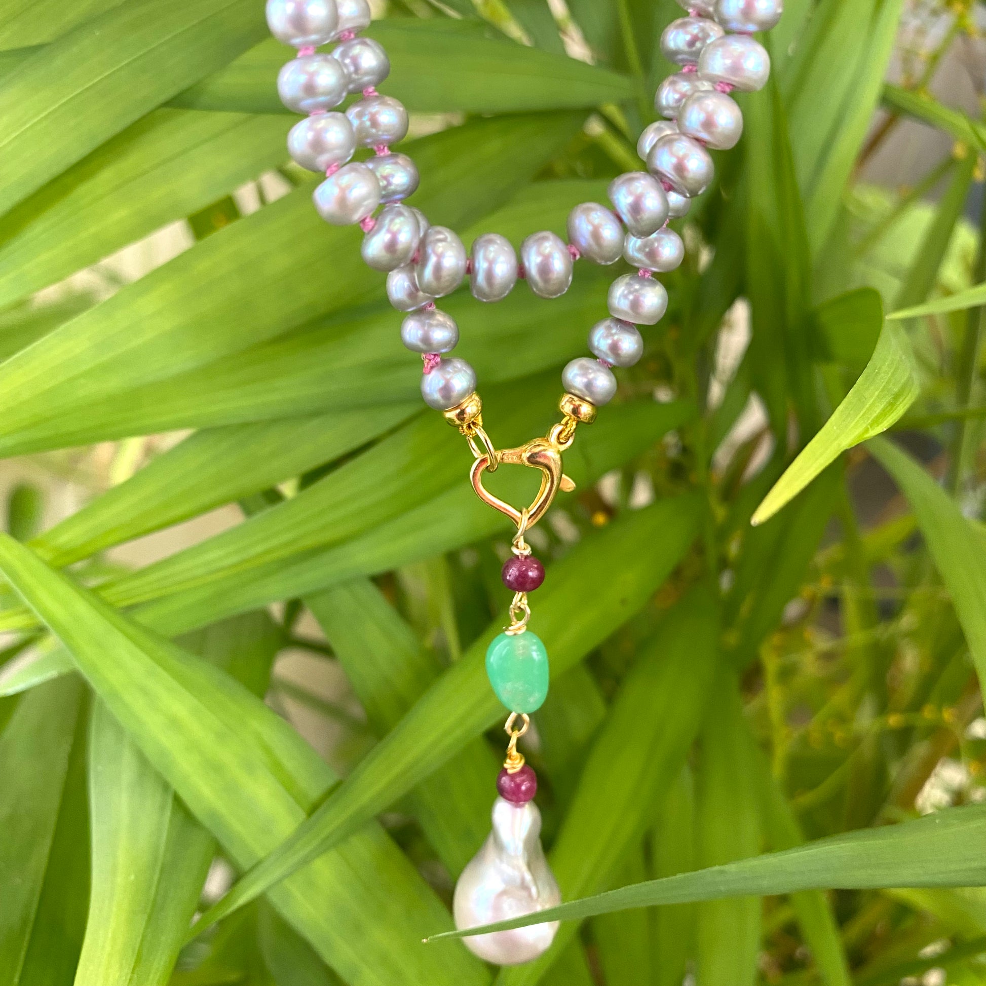 Grey pearl necklace with ruby and chrysoprase pendant on a green background, showcasing elegant craftsmanship.