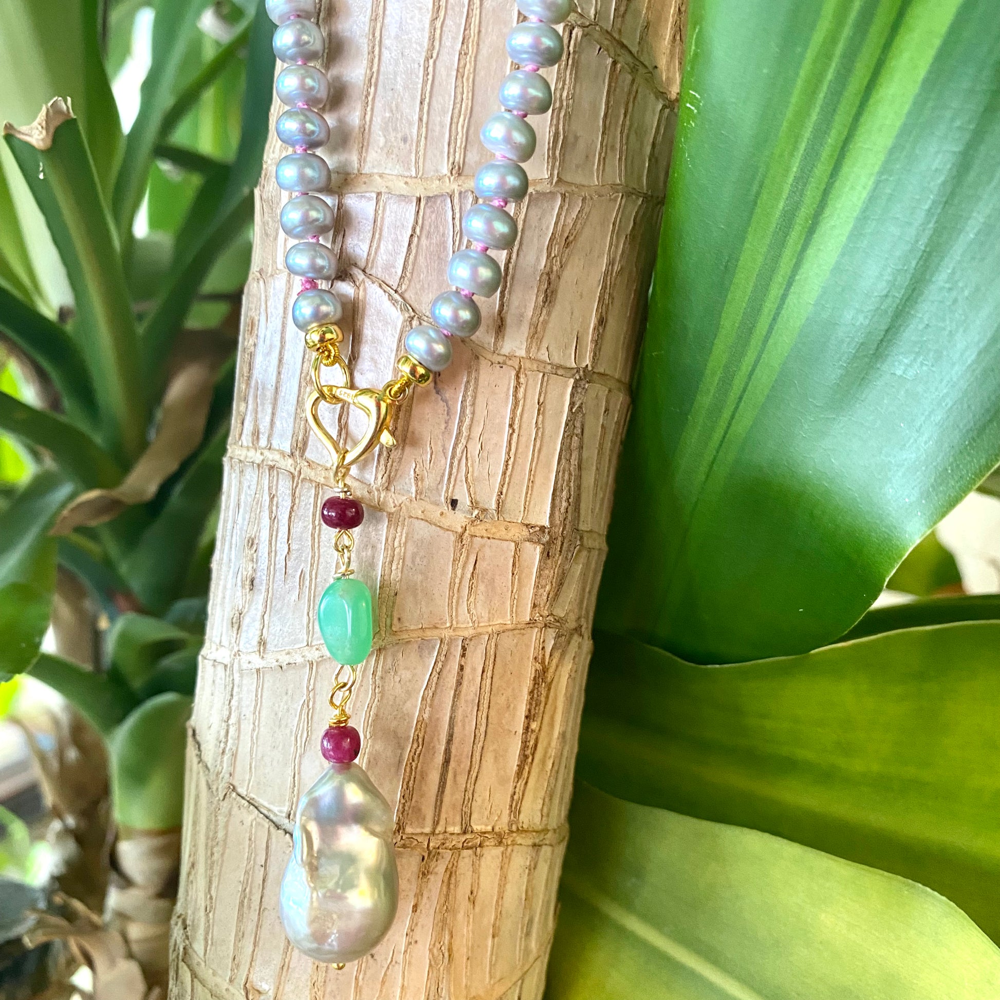 Grey pearl necklace with ruby and chrysoprase pendant on a natural setting.