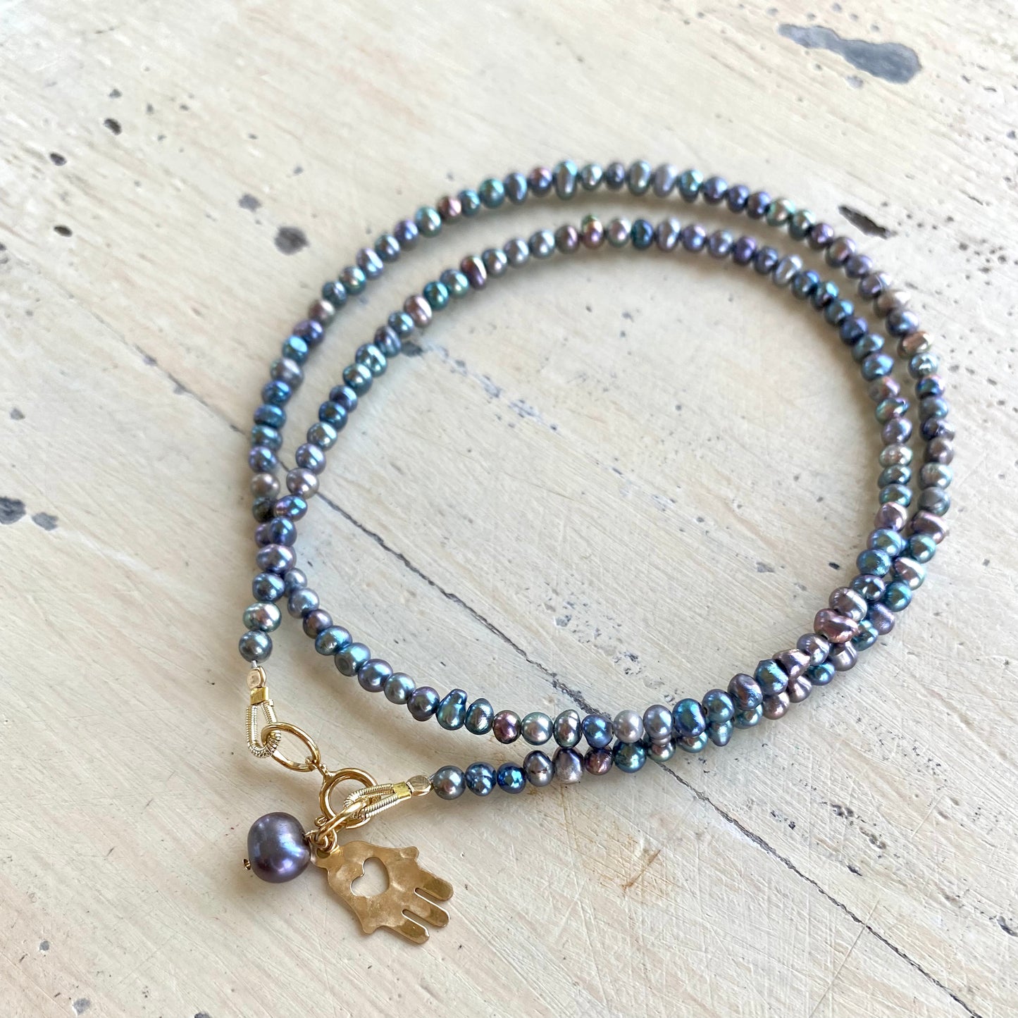 Black pearl hamsa necklace laid flat with mini rice pearls and gold filled hamsa charm, handmade Canadian jewelry