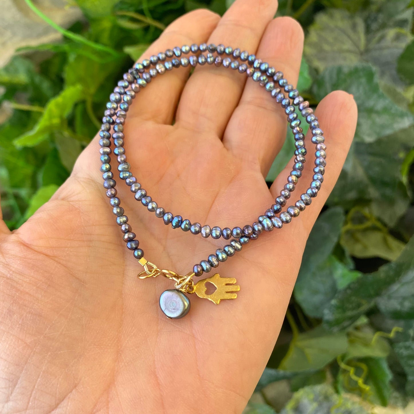 Black pearl hamsa necklace held in hand showing mini rice pearls and gold filled details, handmade in Canada