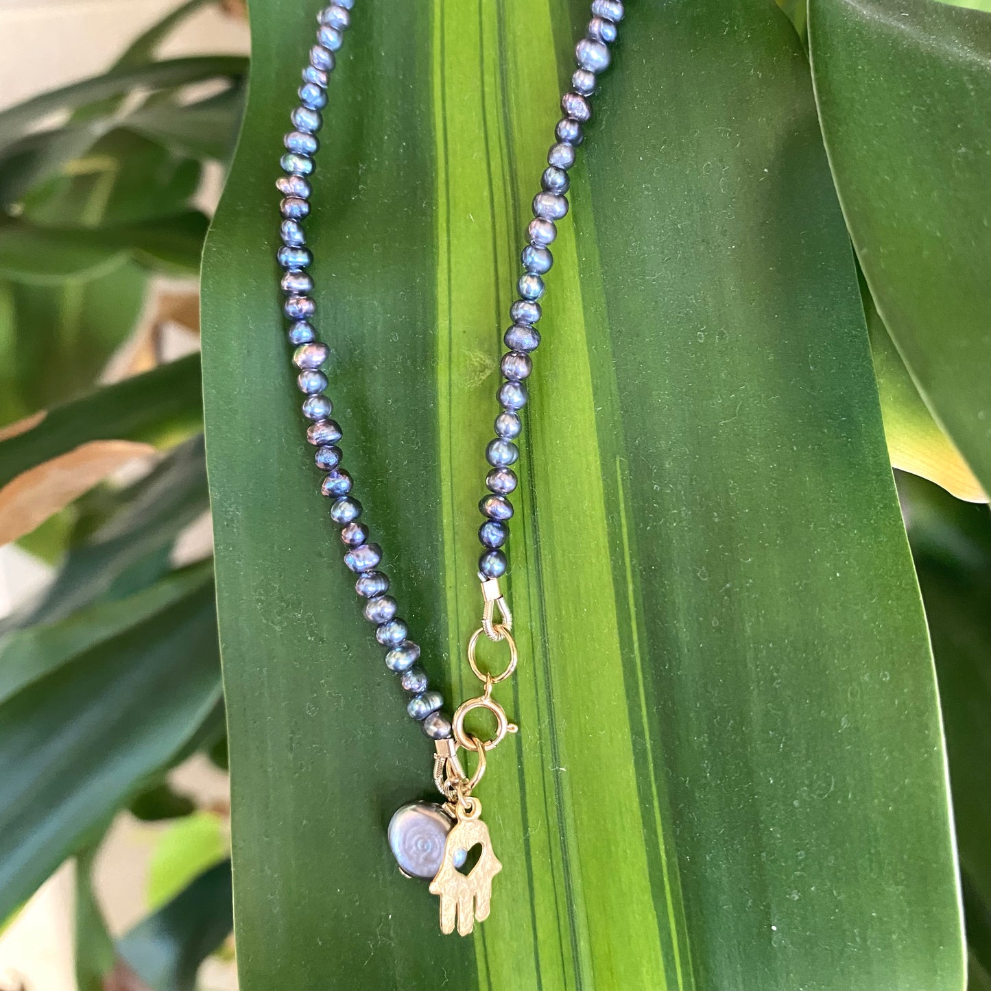 Black pearl hamsa necklace displayed outdoors with gold filled charm, handmade Canadian jewelry