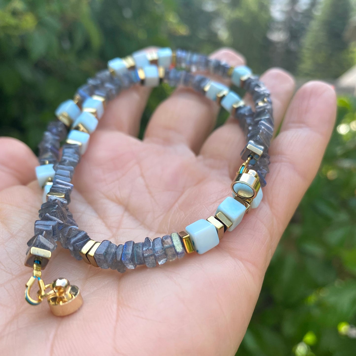 Labradorite and Blue Peru Opal Necklace in hand against greenery, beaded strand with magnetic clasp