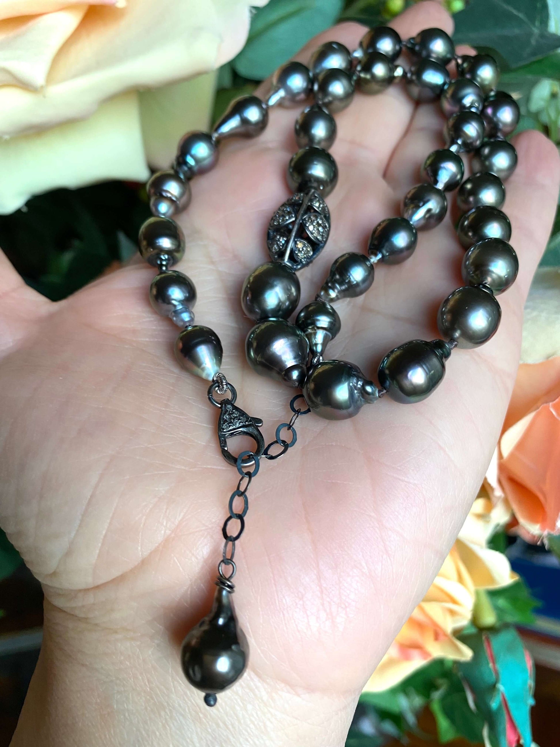 Tahitian baroque pearl necklace with champagne diamonds displayed in hand among blooming roses.