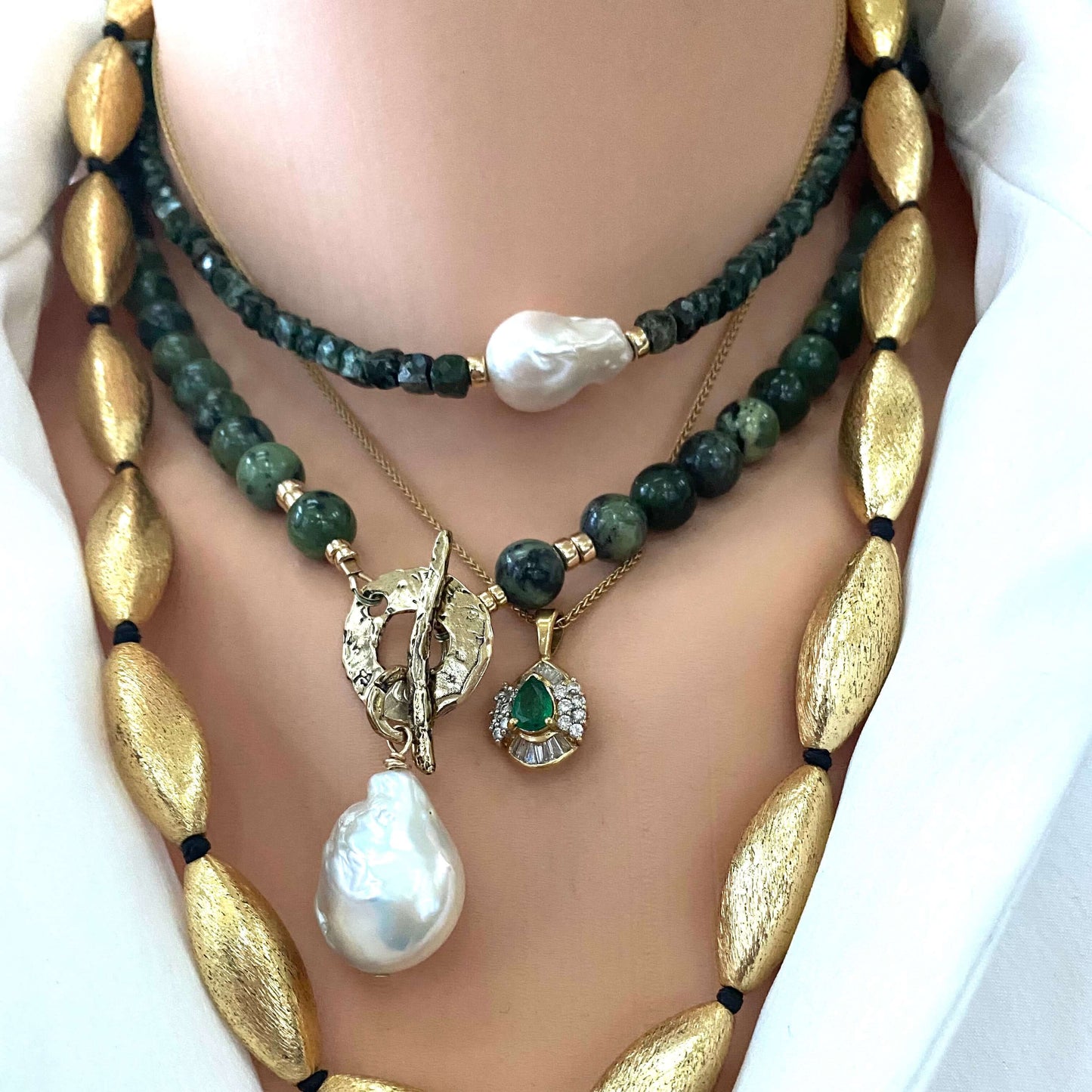 Mannequin wearing a stack of gold, green, and pearl necklaces.