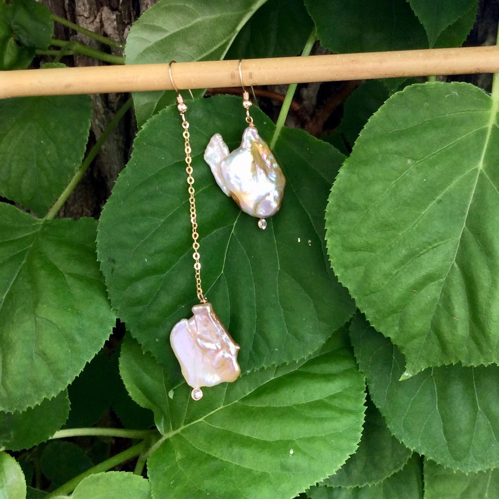 Mismatched Pearl Drop Earrings featuring asymmetrical lengths and gold detailing on green foliage background.